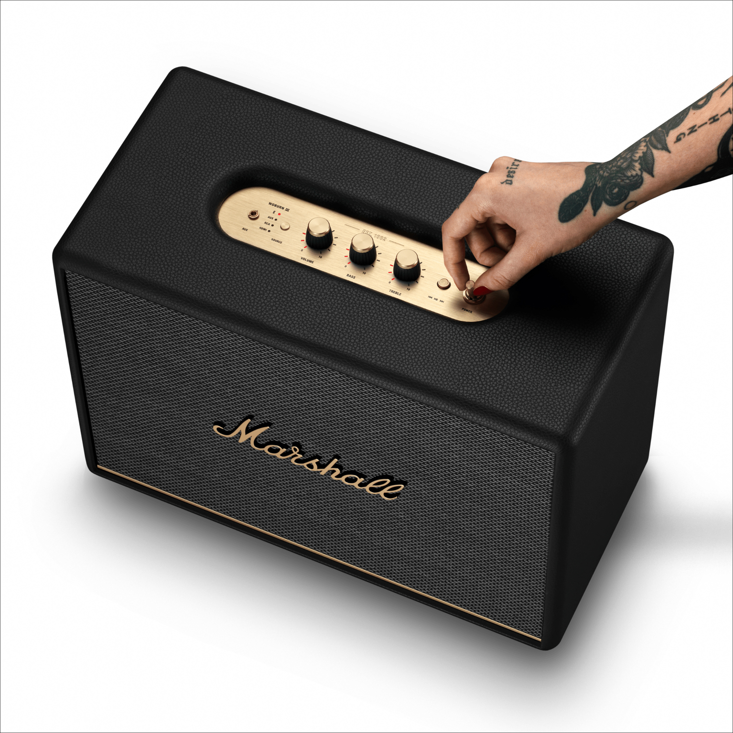 Altavoz Marshall negro con detalles dorados y una mano ajustando el botón de volumen.