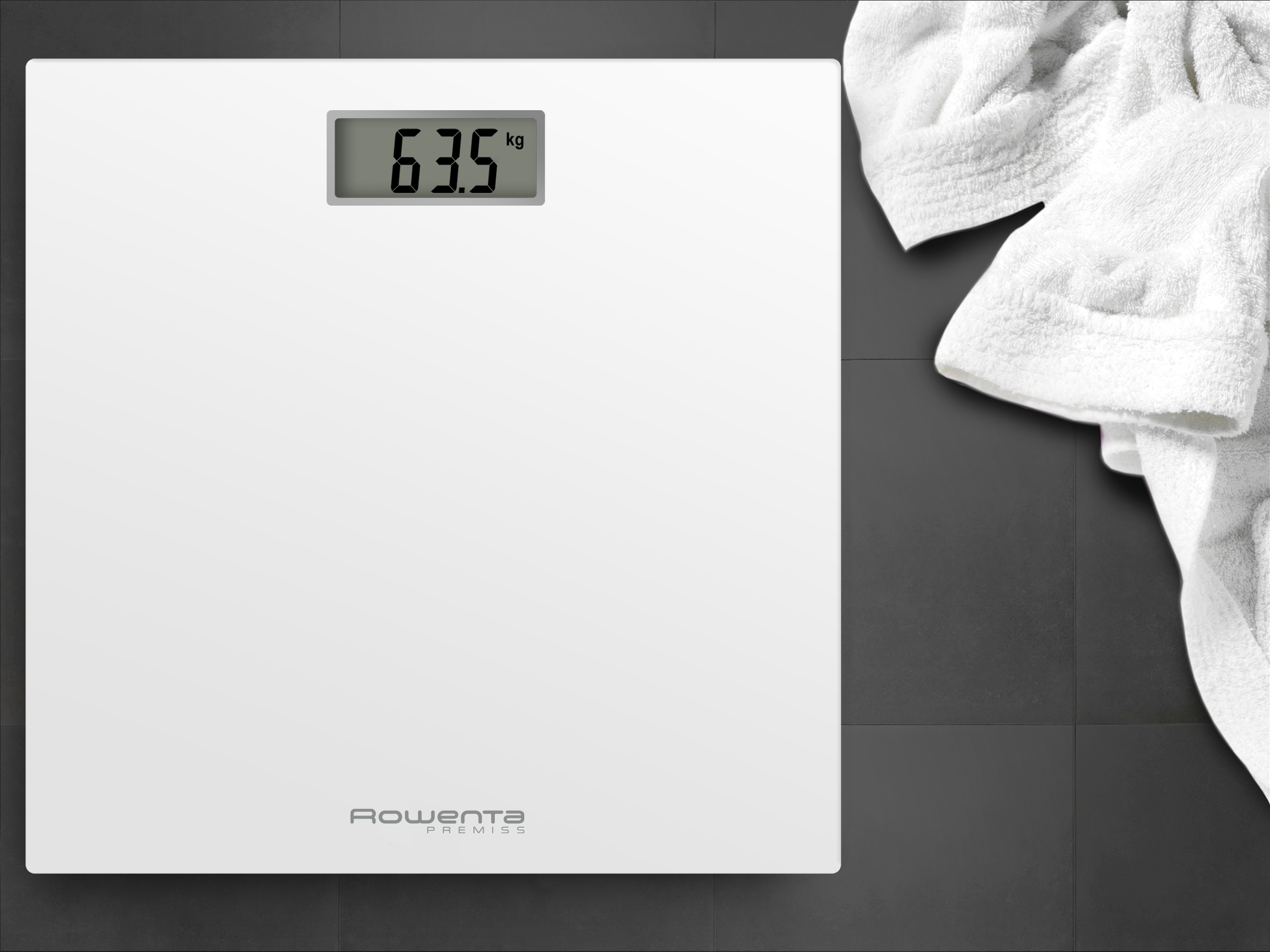 Una báscula digital blanca con el número 63,5 kg, junto a una toalla blanca sobre un suelo de baldosas oscuras.