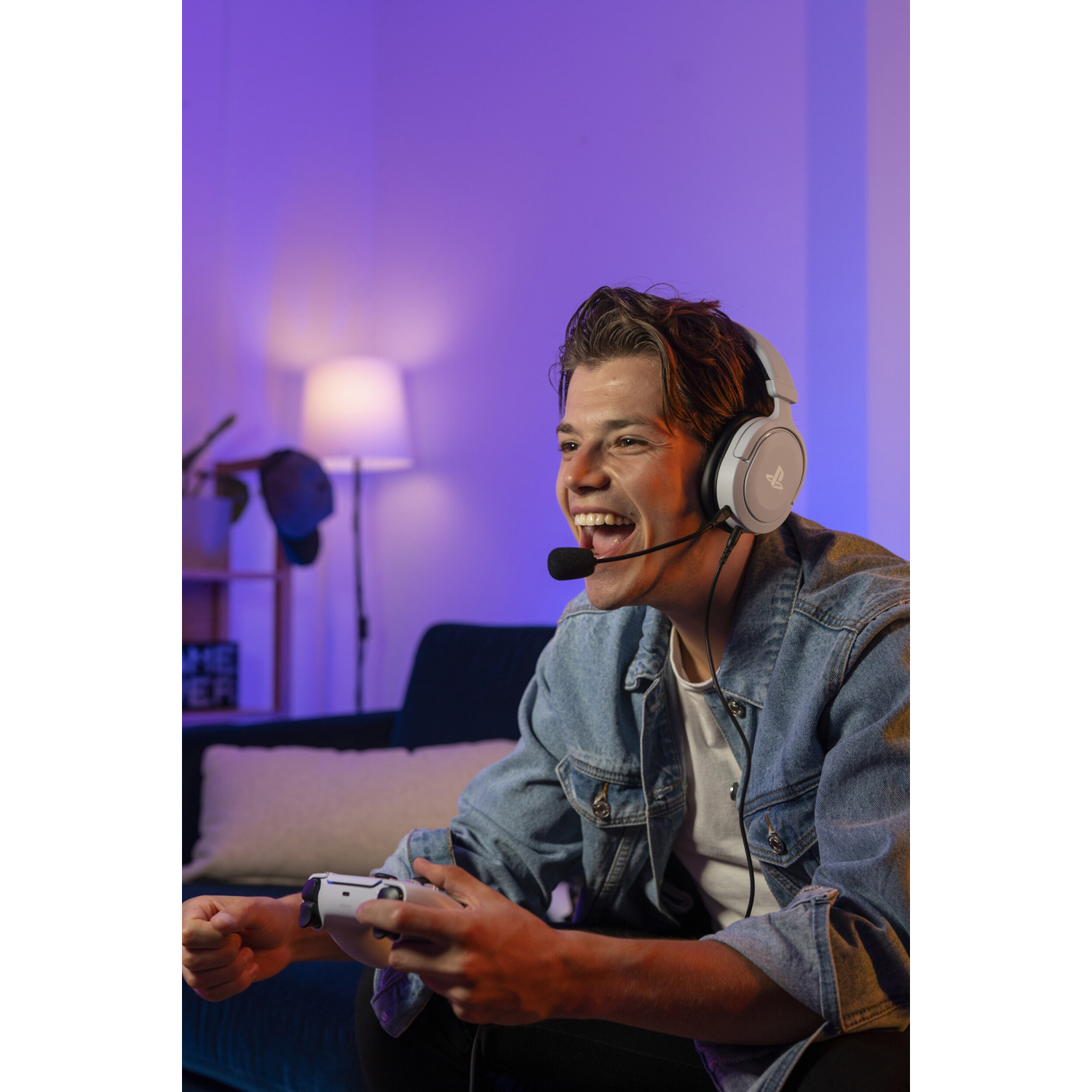 Giovane con cuffie e giacca di jeans, gioca a un videogioco e sorride.