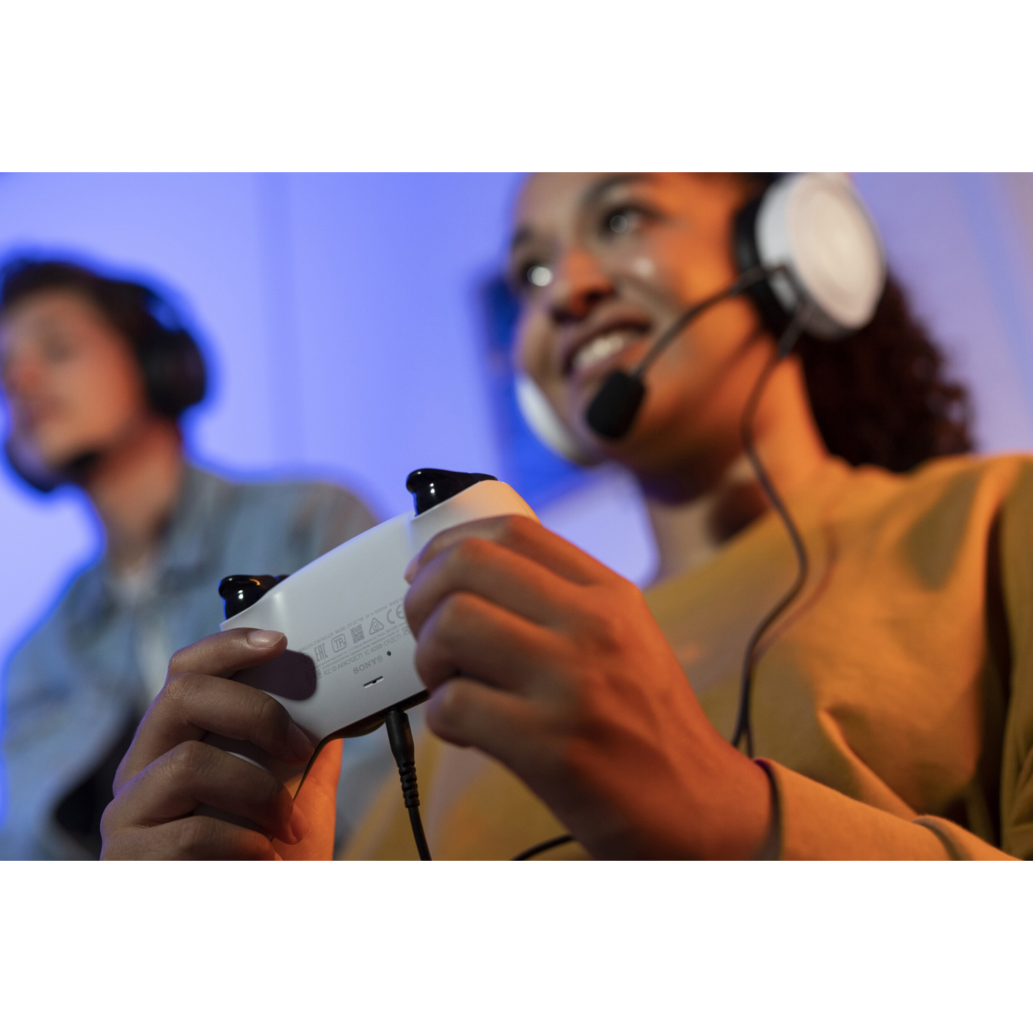 Una donna sorride, tenendo in mano un controller di gioco bianco, con un auricolare.