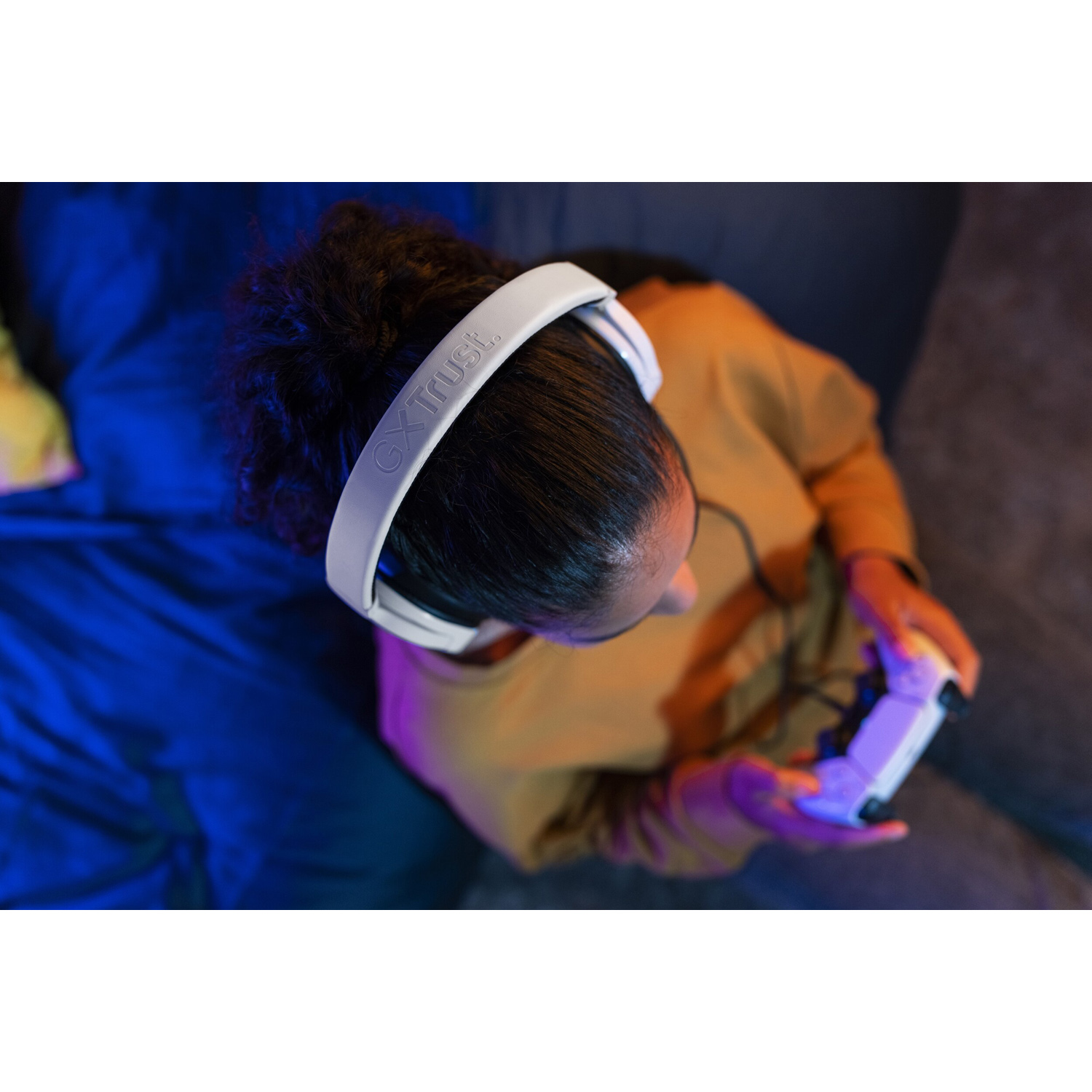 Persona con cuffie bianche gioca con un controller, seduta su un divano. Luci blu e viola.