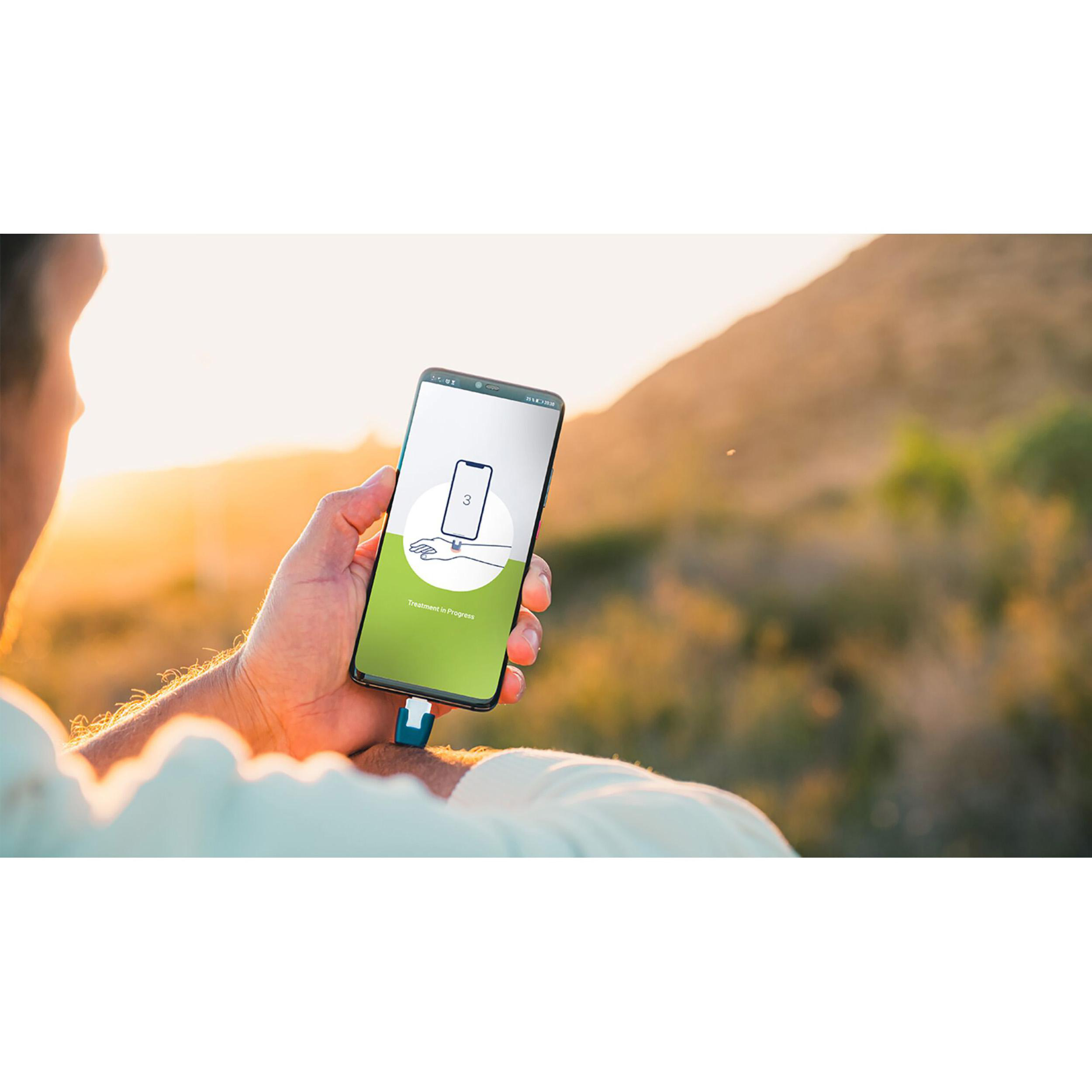 Eine Person hält ein Smartphone mit App-Bildschirm. Der Hintergrund zeigt einen Sonnenuntergang.