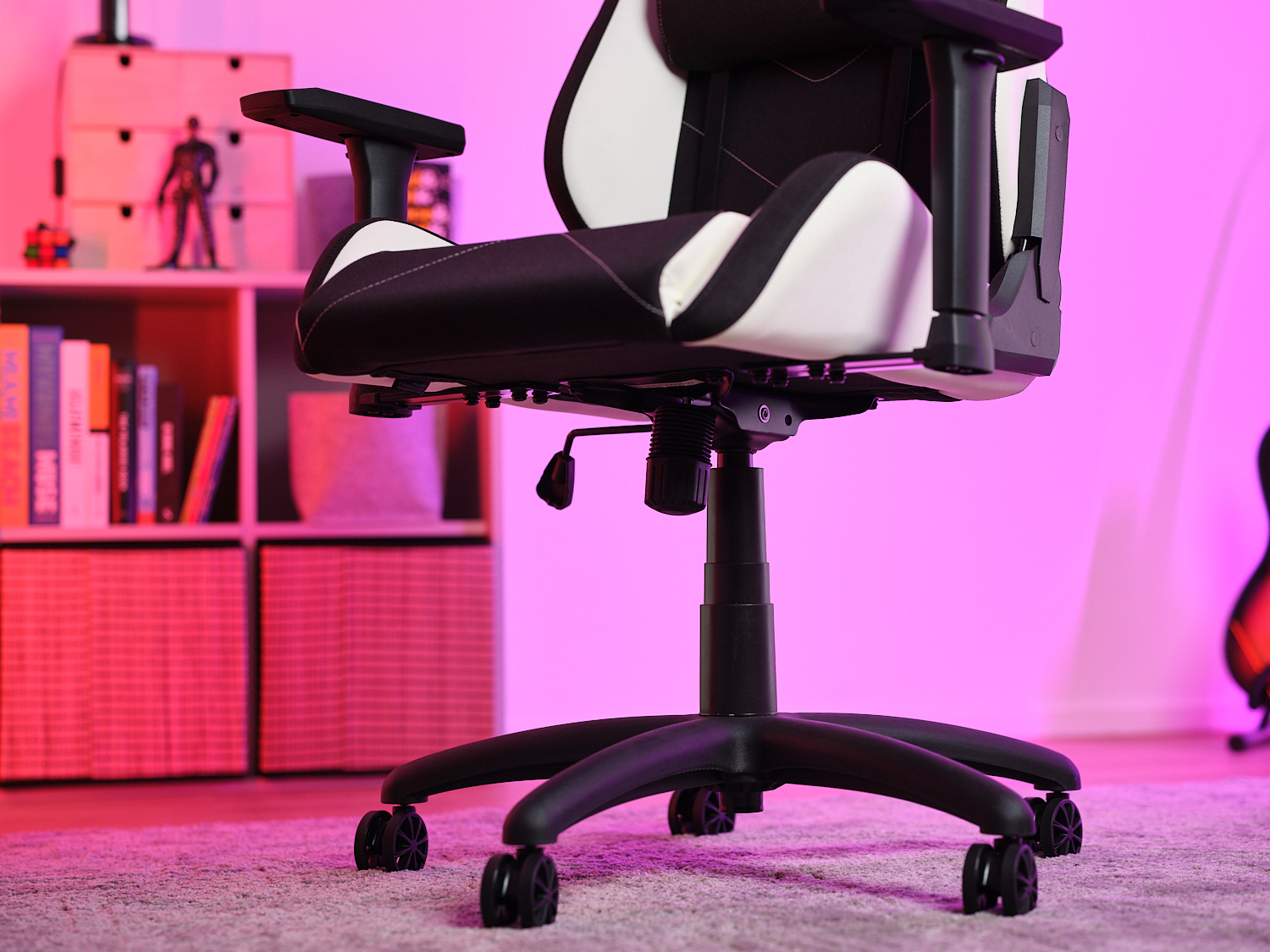 Una sedia da gioco nera e bianca su un tappeto in una stanza con illuminazione rosa e una libreria sullo sfondo.