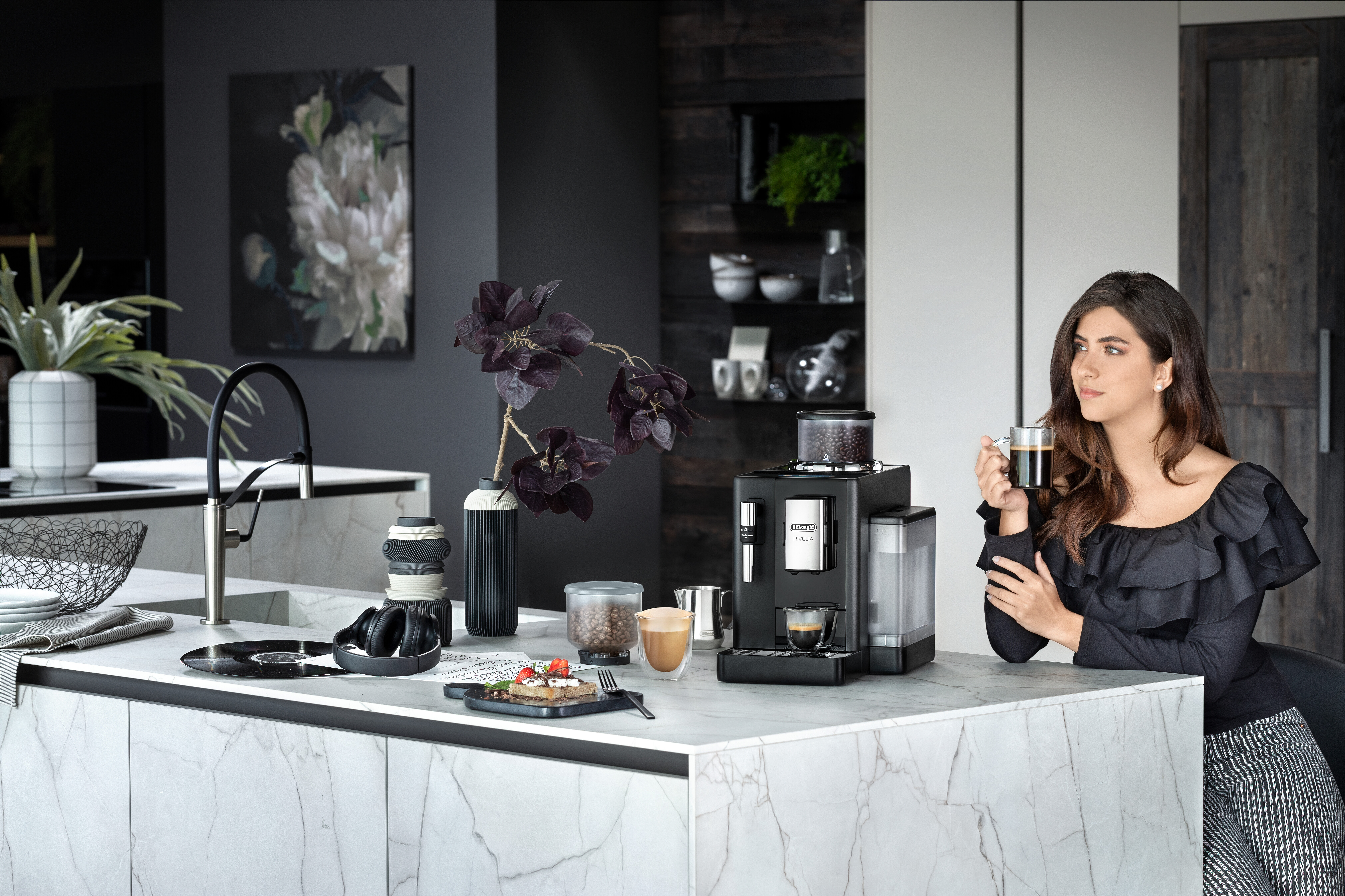 Frau mit Kaffee trinkt aus einer schwarzen Kaffeemaschine auf einer Marmorarbeitsplatte.