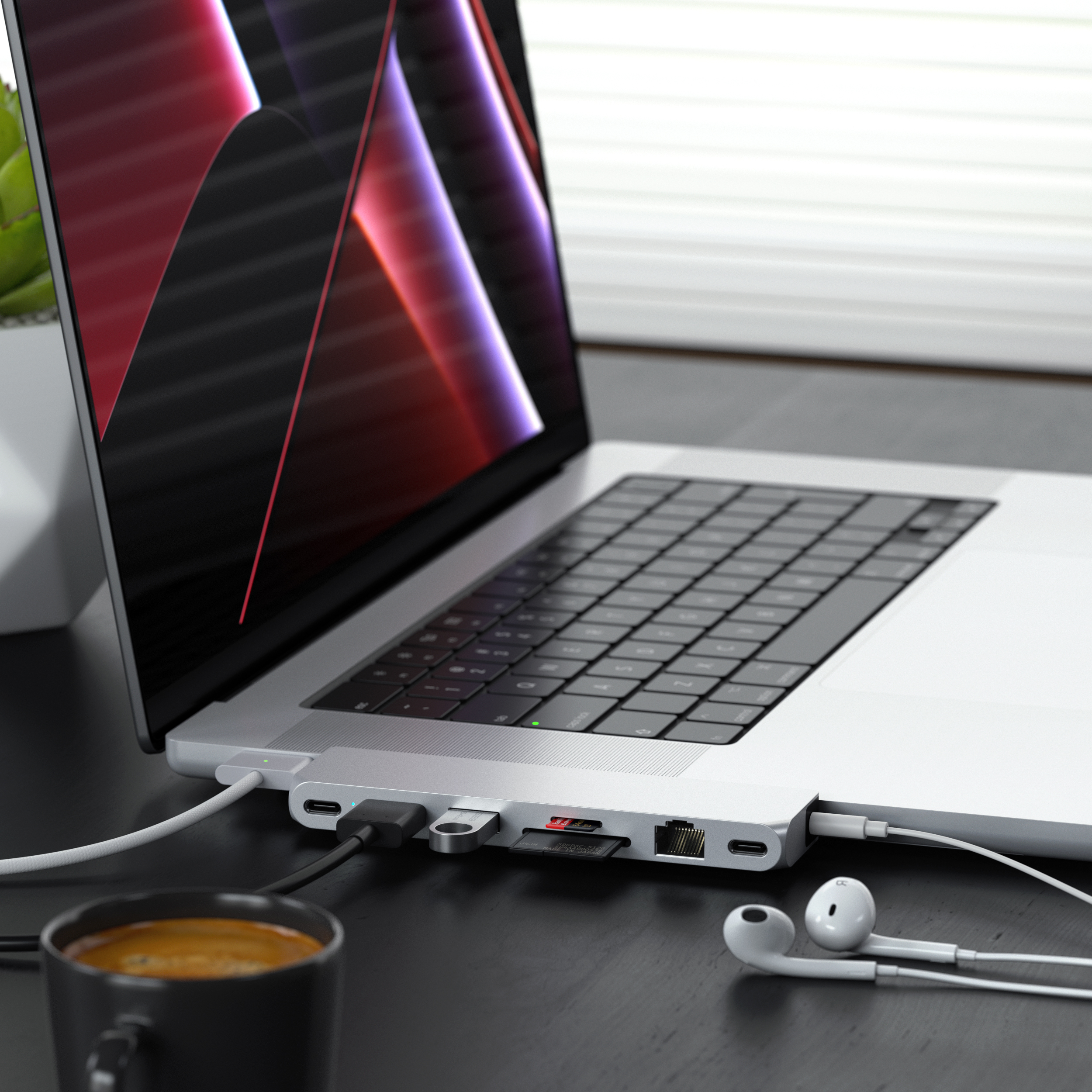 Egy laptop egy többportos adapterhez csatlakoztatva. Egy csésze kávé és fülhallgató van mellette.