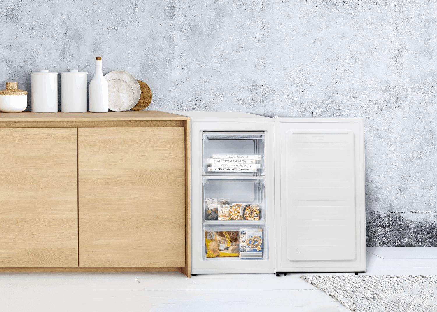 Congelador blanco con puerta abierta, estantes de comida congelada, al lado de un mueble.