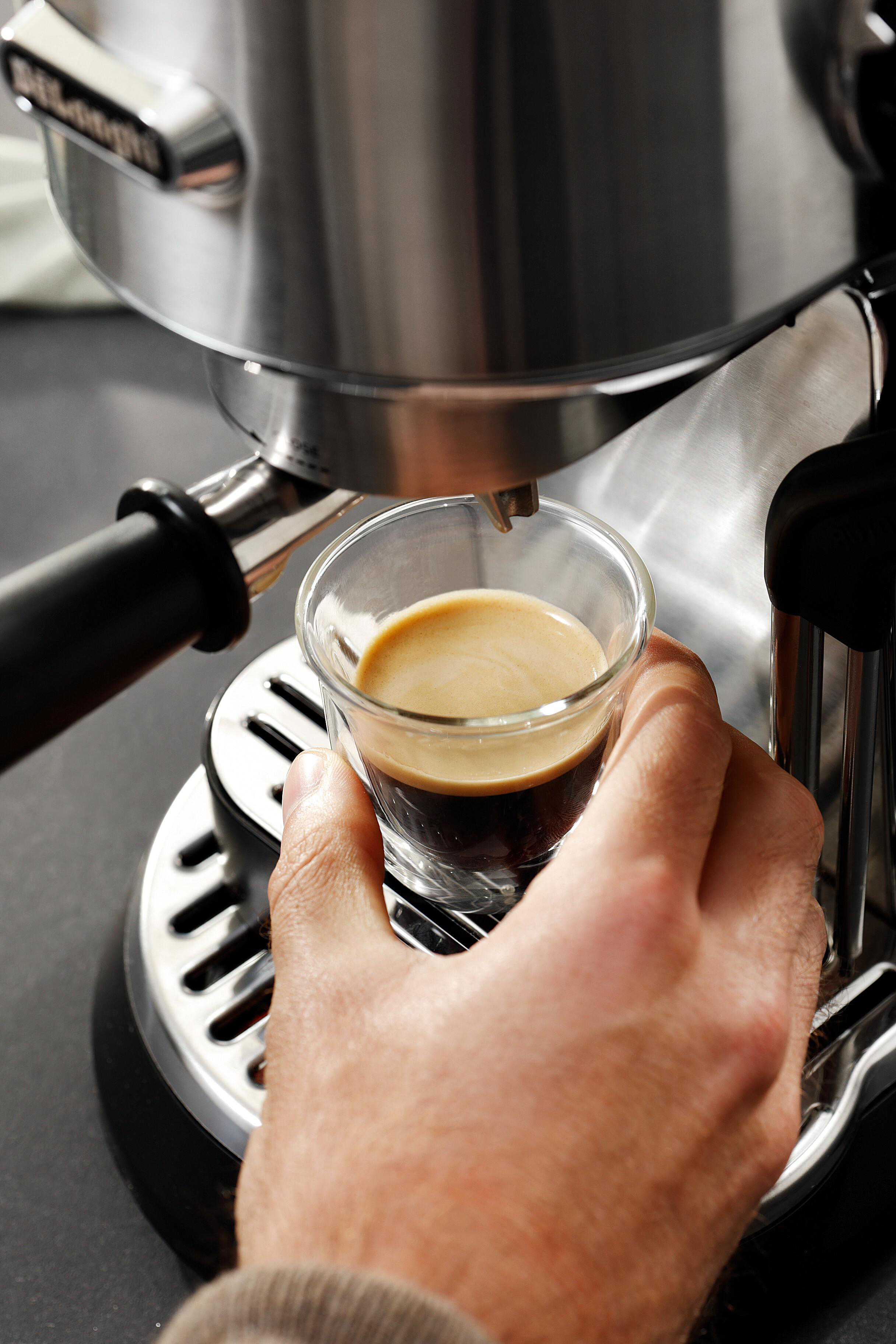 Eine Hand hält ein Glas Espresso neben einer Espressomaschine.