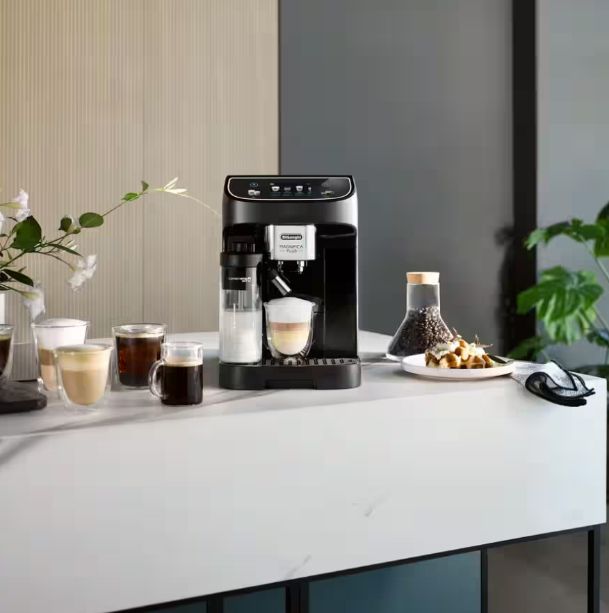 Schwarze Kaffeemaschine mit Milchaufschäumer und mehreren Kaffeegläsern auf weißer Arbeitsplatte. Der Hintergrund ist neutral.