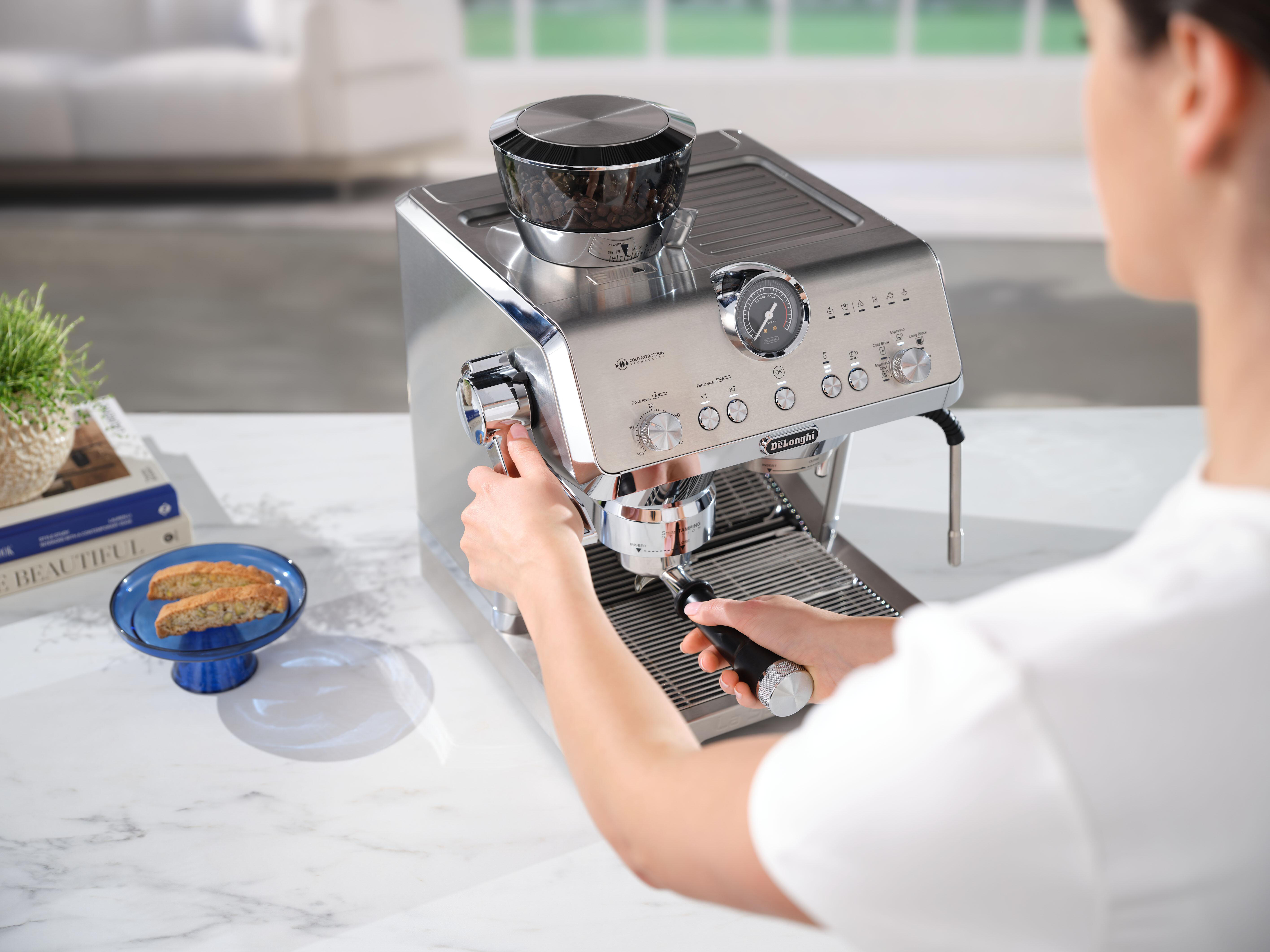 Eine Frau benutzt eine Espressomaschine. Die Maschine ist aus Edelstahl mit einem Bohnenmahler oben.