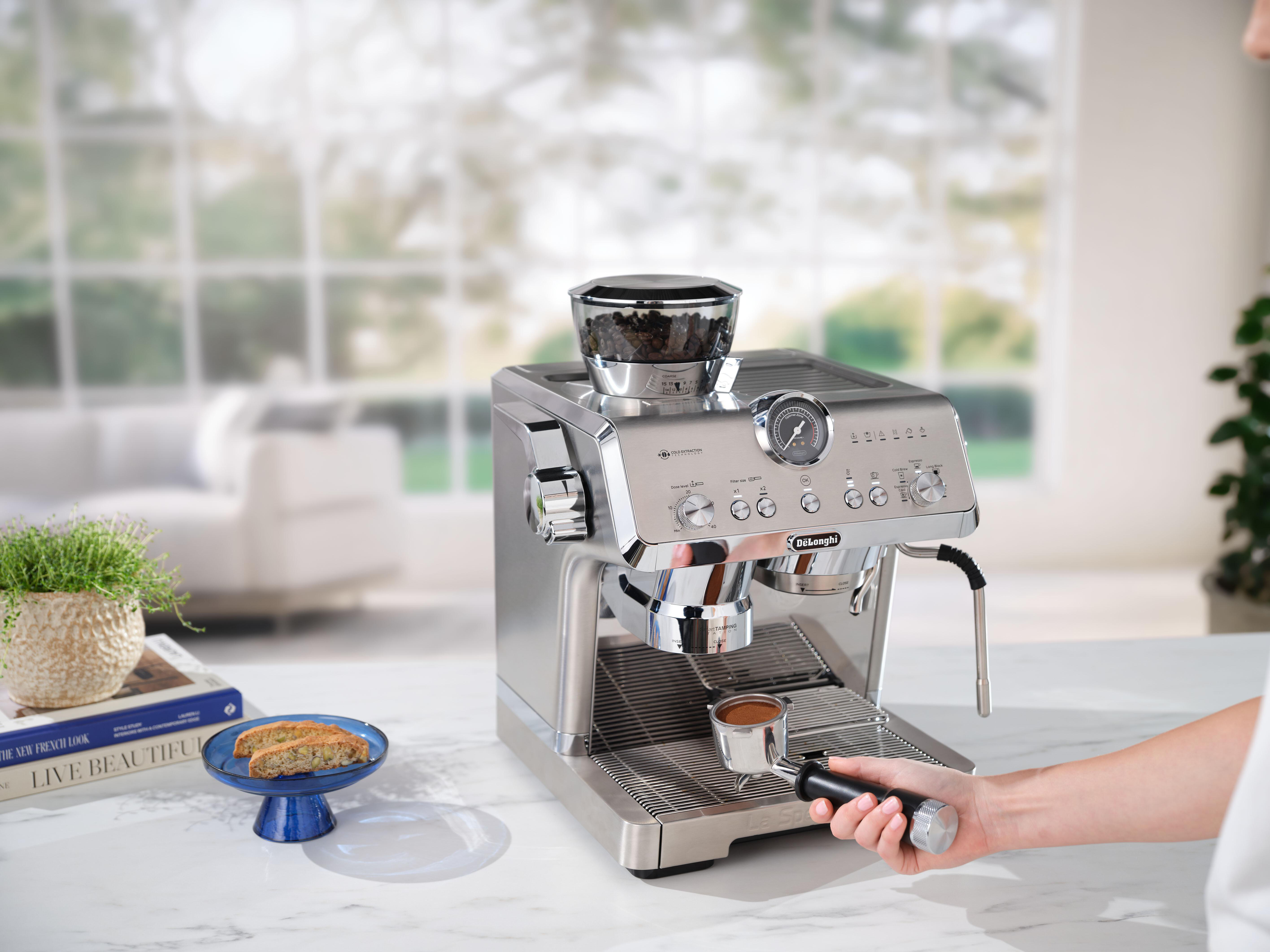 Silberne De'Longhi Espressomaschine mit Kaffeetasse. Eine Person bedient die Maschine.