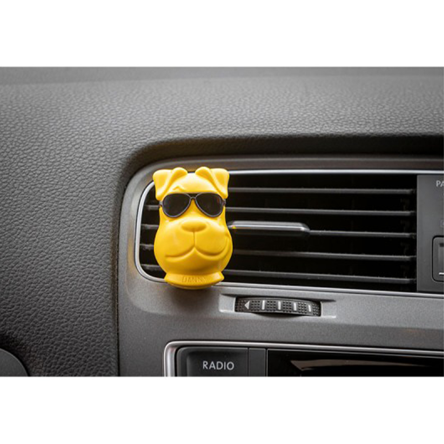 Un deodorante per auto giallo a forma di cane con occhiali da sole sul cruscotto.