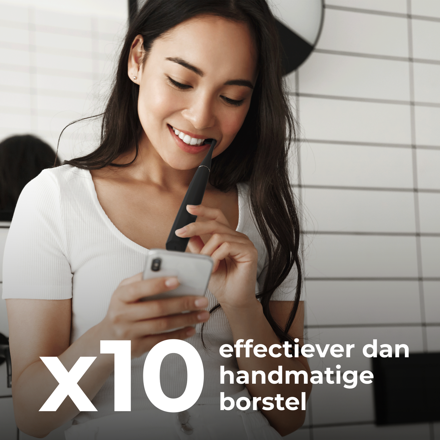 A woman smiling while using an electric toothbrush and holding her phone.