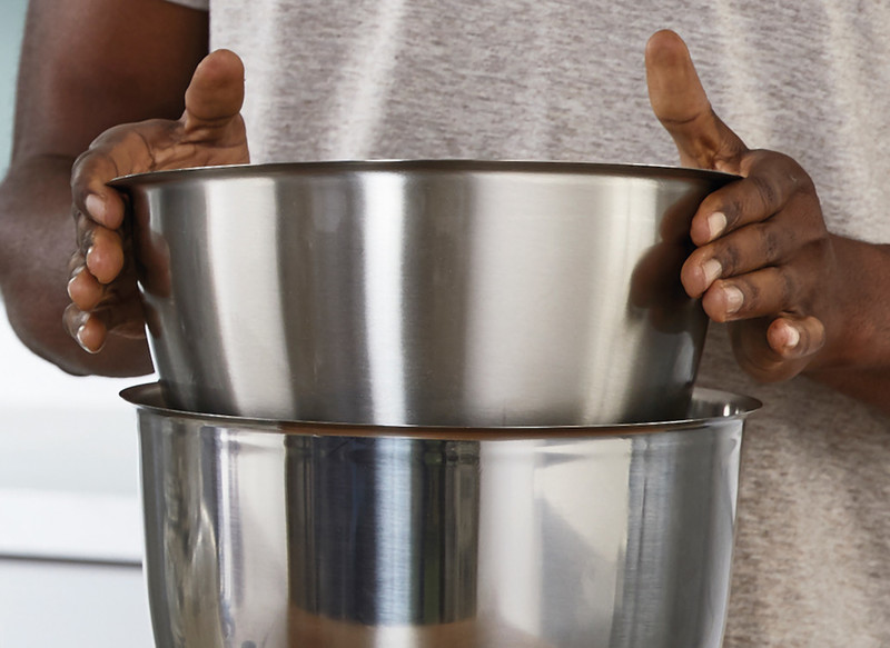 Dłonie trzymające dwie miski ze stali nierdzewnej. Jedna miska jest włożona do drugiej. Szare tło koszuli.