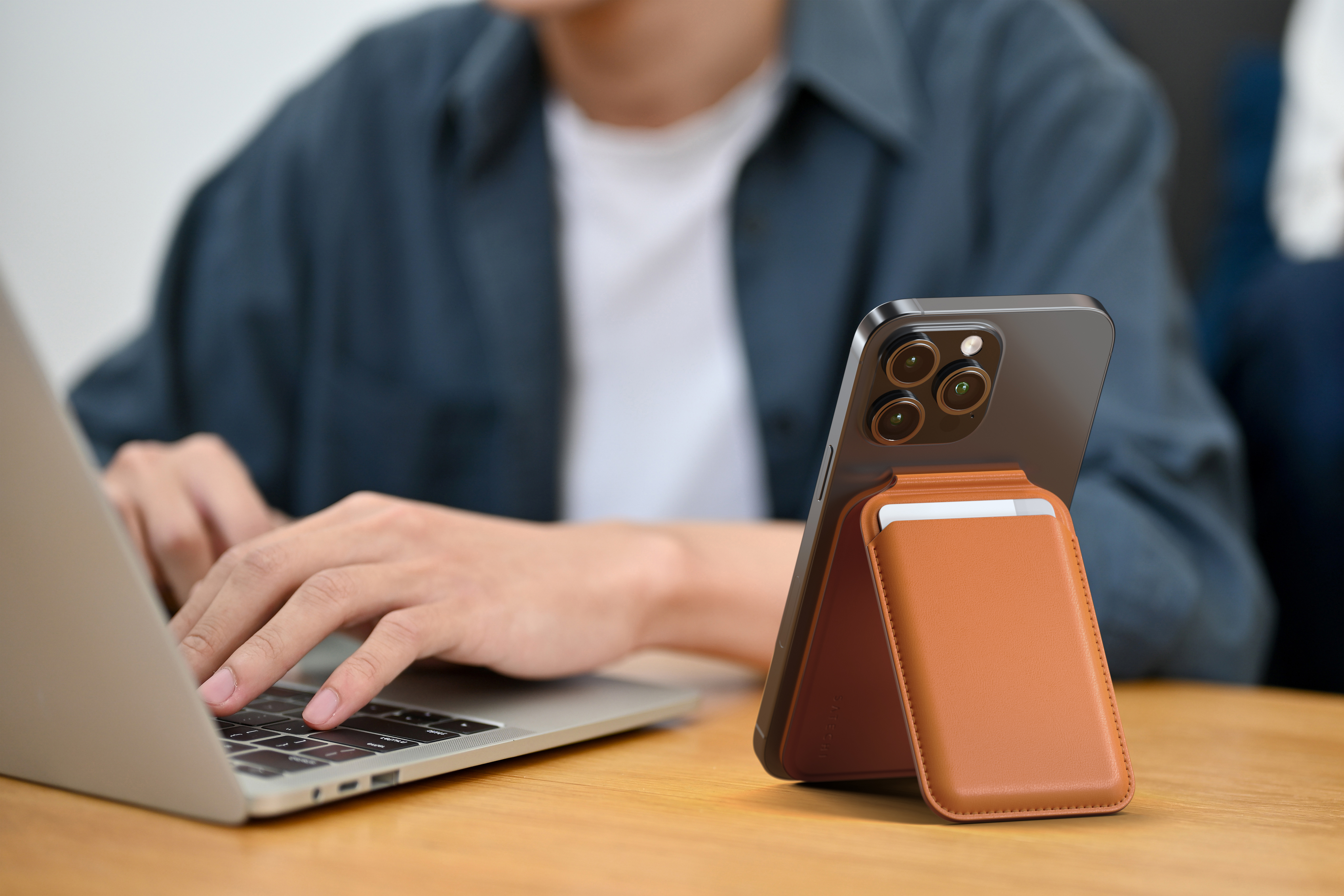 Egy személy laptopot használ, telefonnal, ami egy állványon van. A telefonnak bőr kártyatartója van.