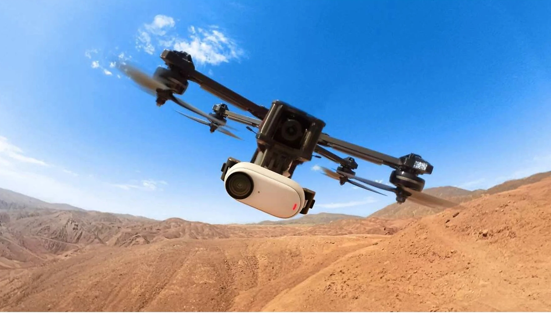 Dron lecący nad pustynnym krajobrazem z niebieskim niebem w tle.