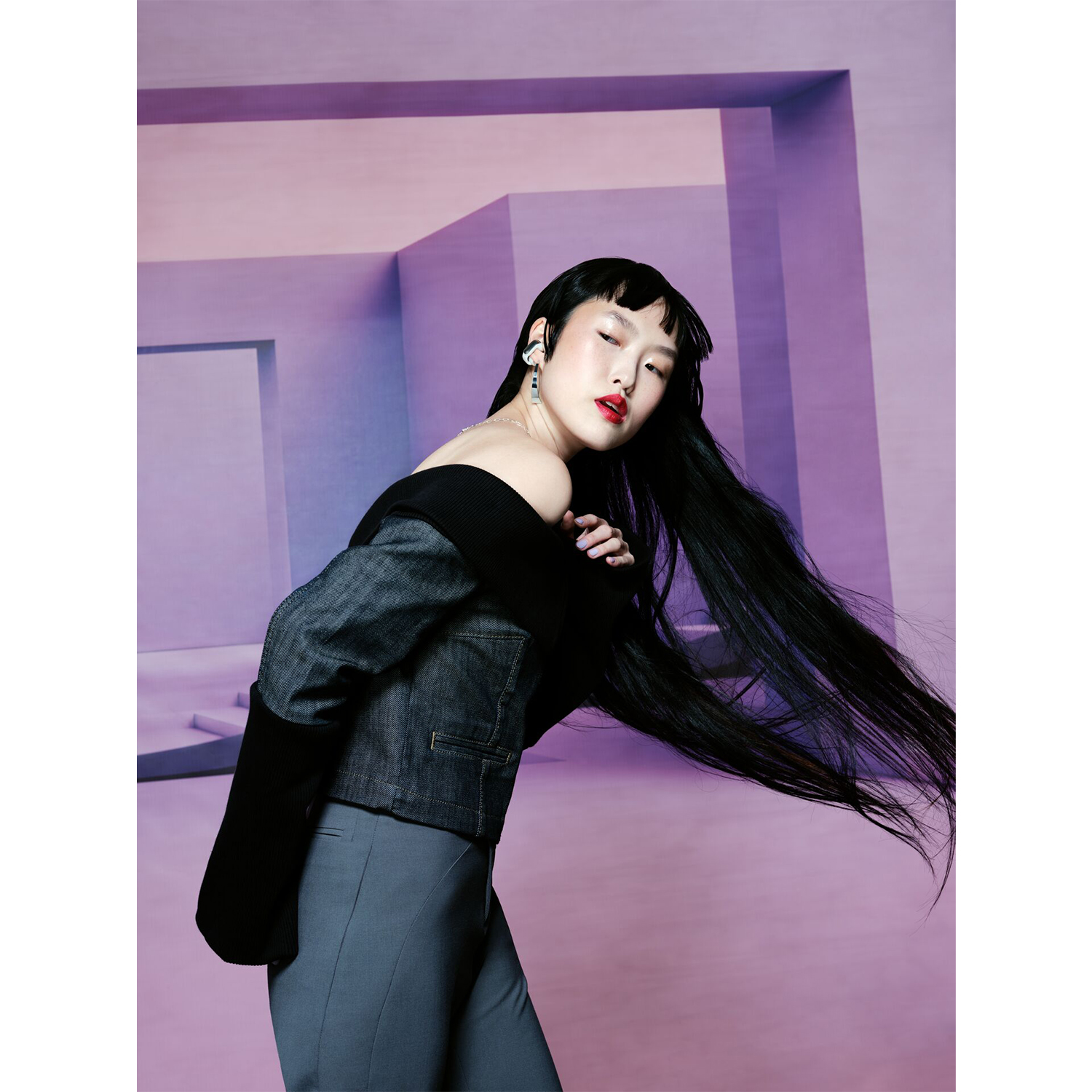 Una donna in un outfit elegante posa in una stanza viola con architettura moderna.
