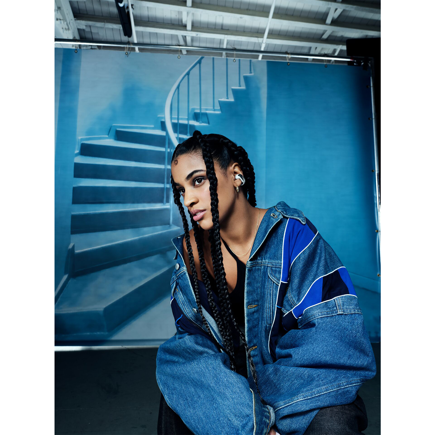 Una donna con trecce indossa una giacca di jeans e orecchini d'argento. Sfondo blu.