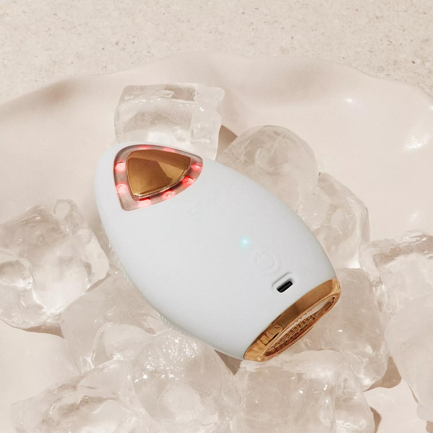 Weißes und goldenes Schönheitsgerät auf Eiswürfeln, rotes Licht leuchtet.