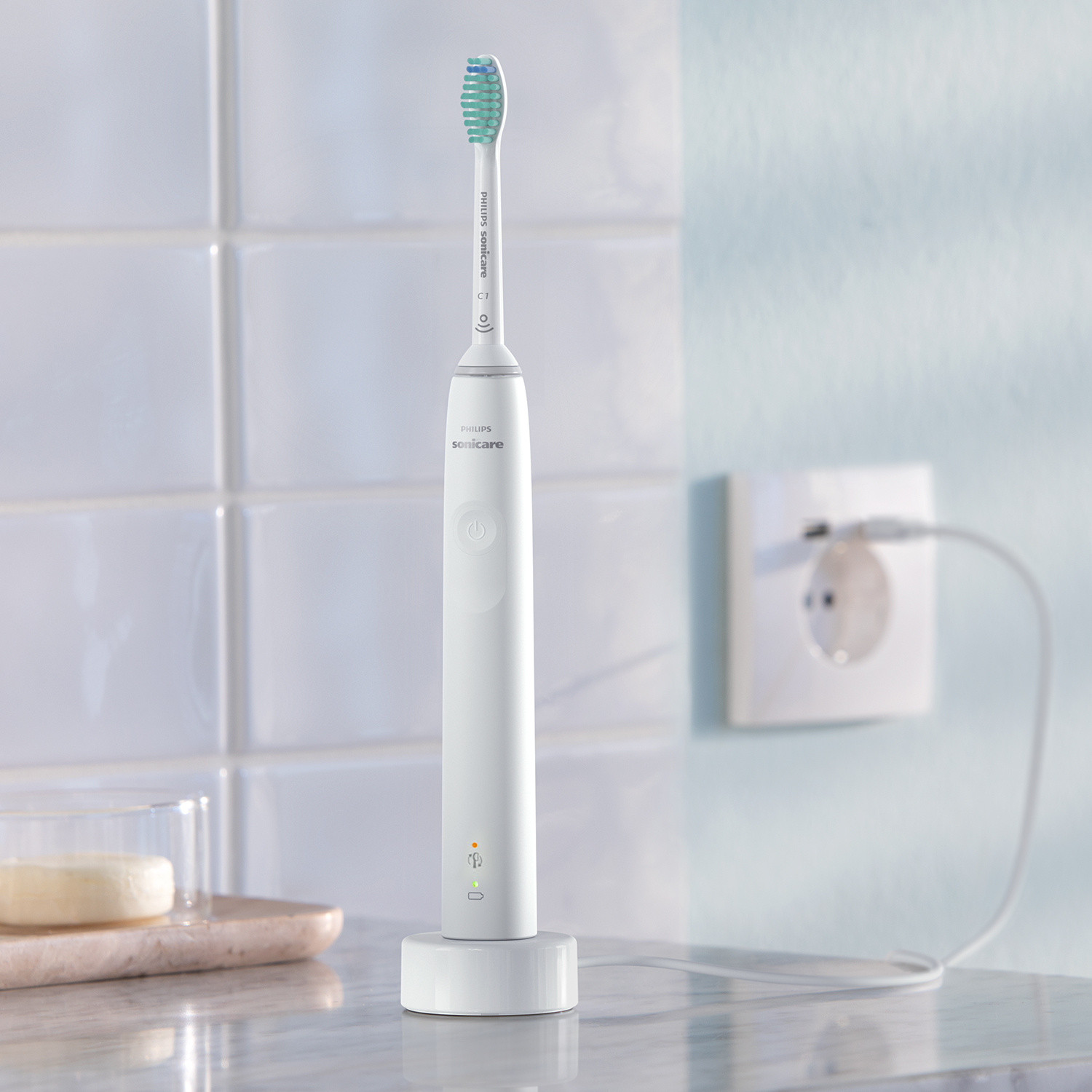 Beyaz bir Philips Sonicare elektrikli diş fırçası, bir prizin yanında bir stand üzerinde şarj oluyor.