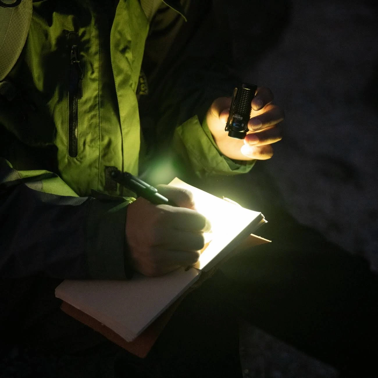 Eine Person schreibt mit einem Stift in ein Notizbuch, beleuchtet von einer kleinen schwarzen Taschenlampe.