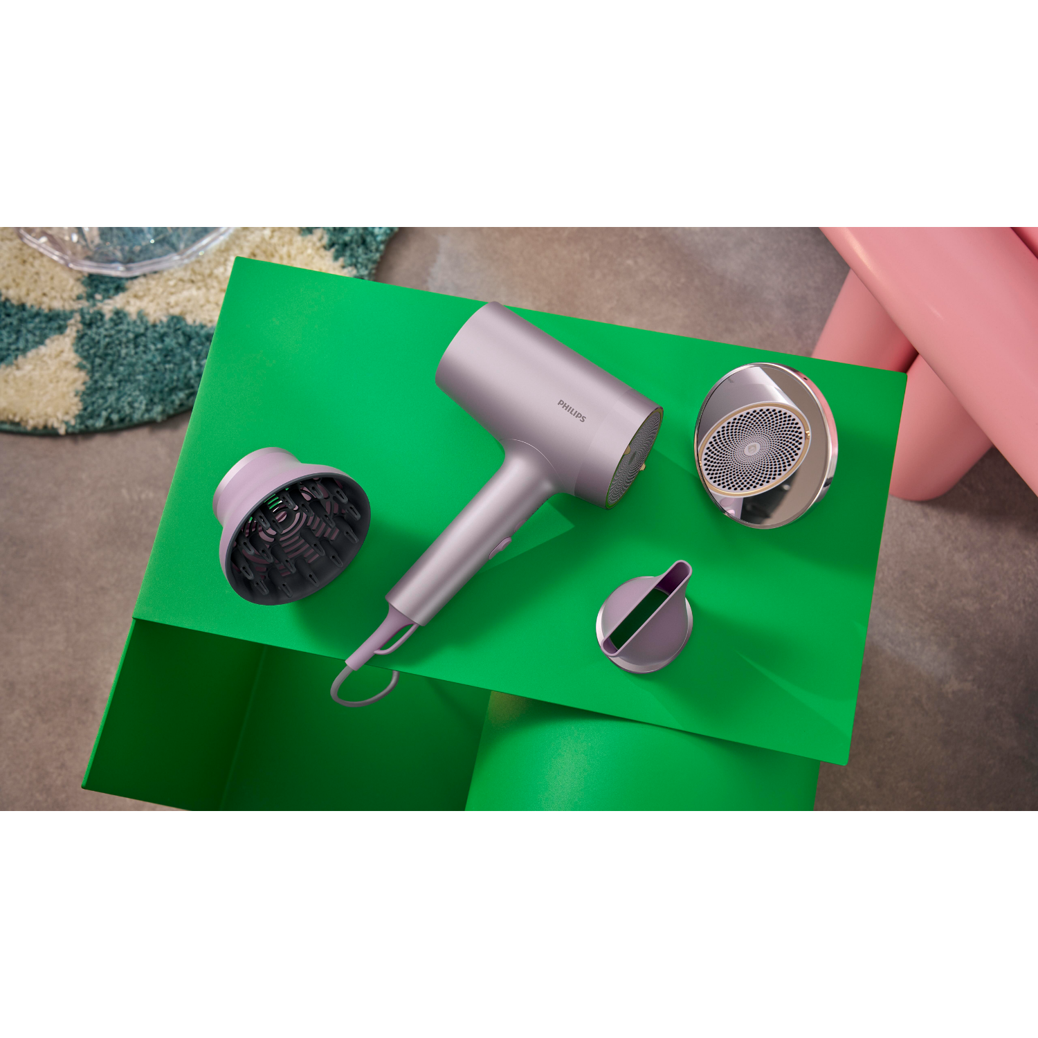 Hair dryer with accessories on a green table with a pink background, studio shot.