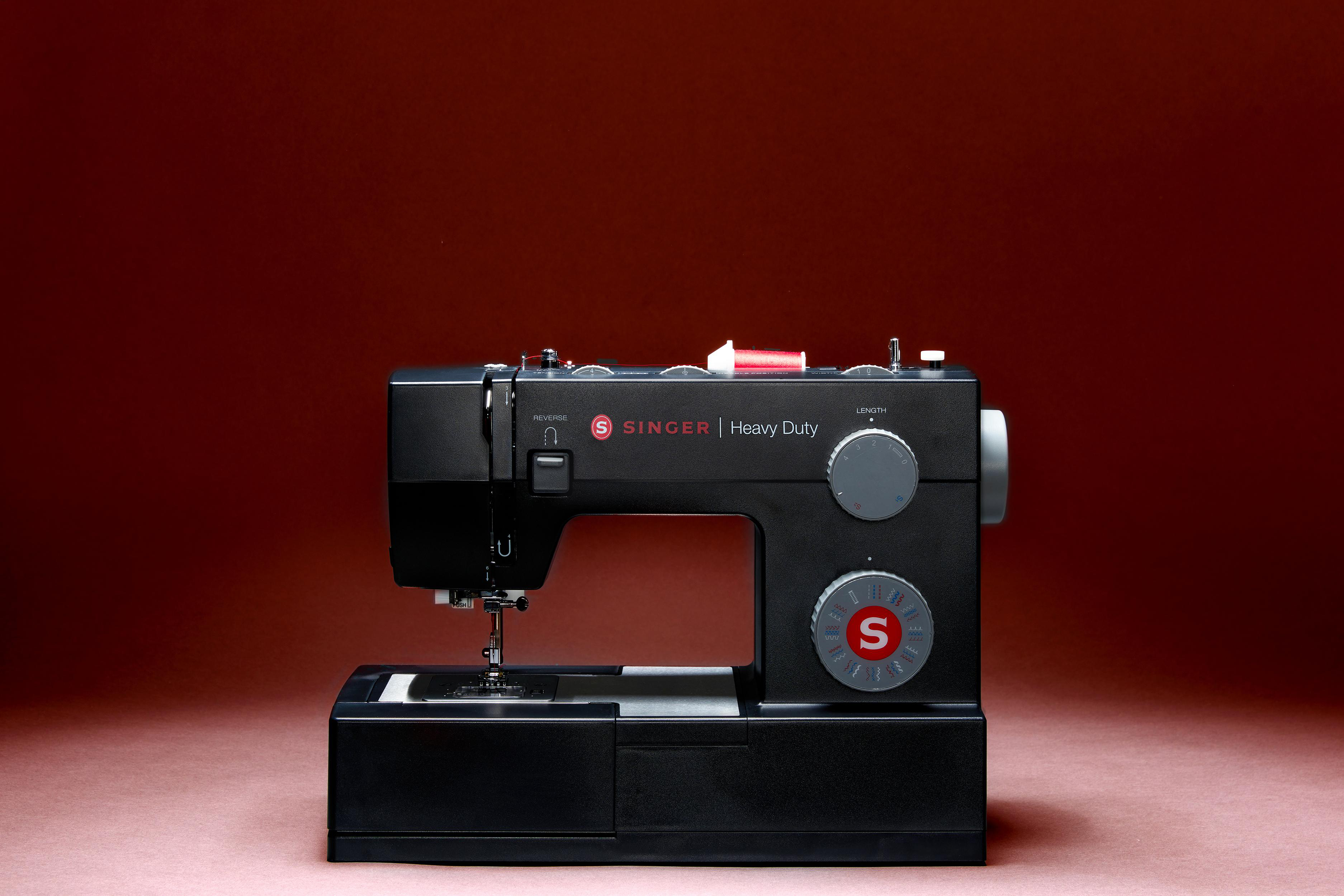Schwarze Singer-Nähmaschine auf rotem Hintergrund. Rote Garnrolle oben.