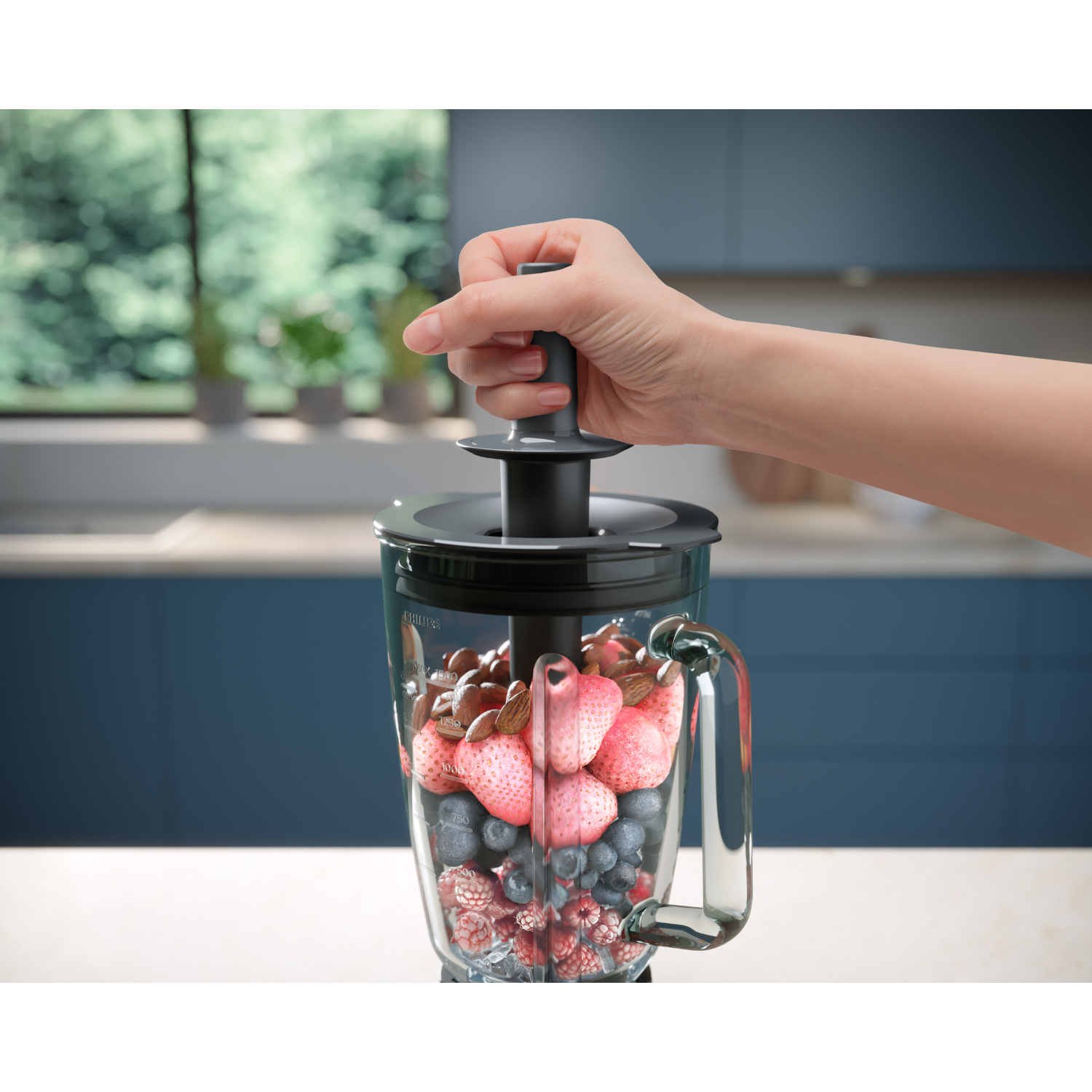 Hand holding a blender lid with a plunger. The jar contains berries and nuts.