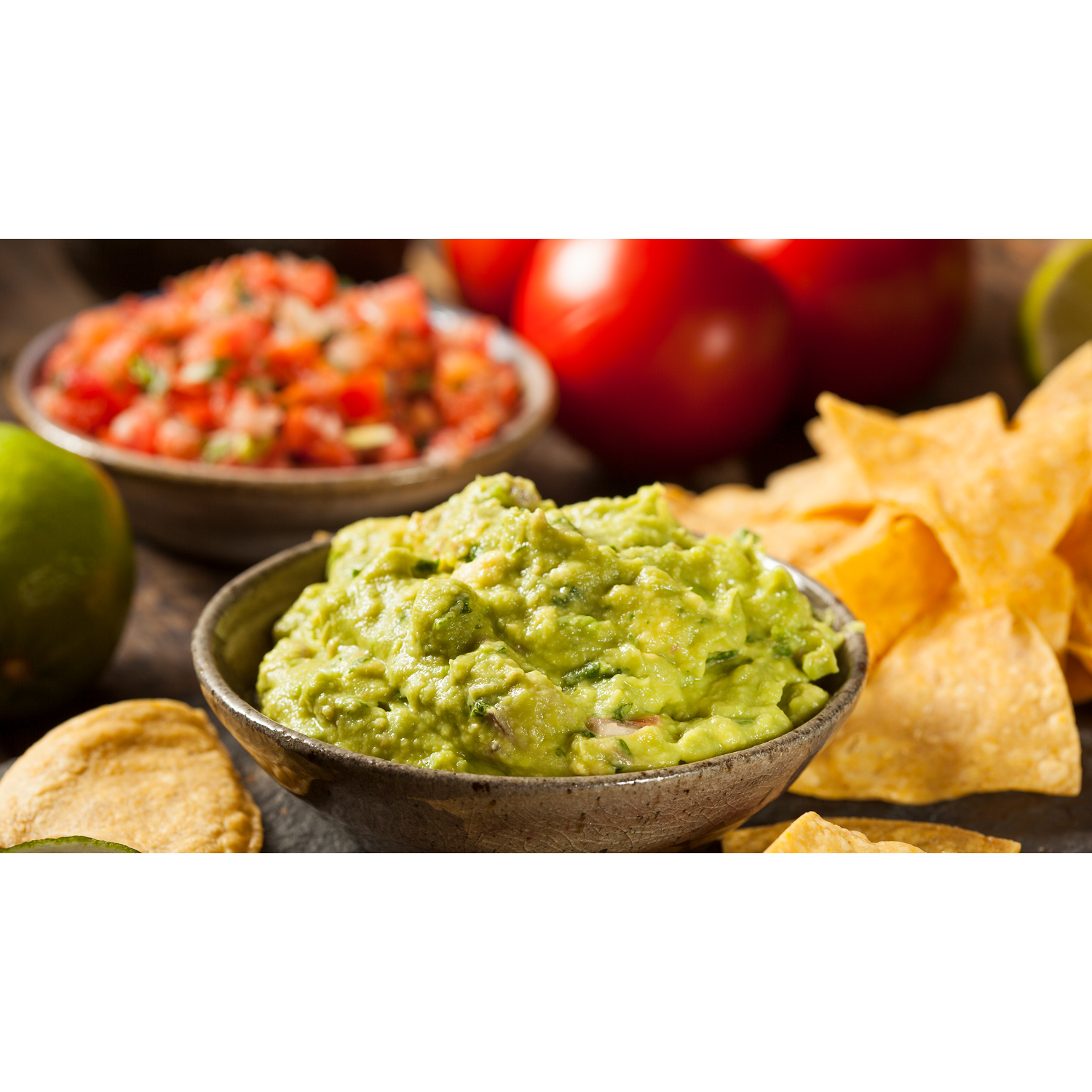 Guacamole in een kom, salsa in een kom, tortillachips en tomaten op hout.