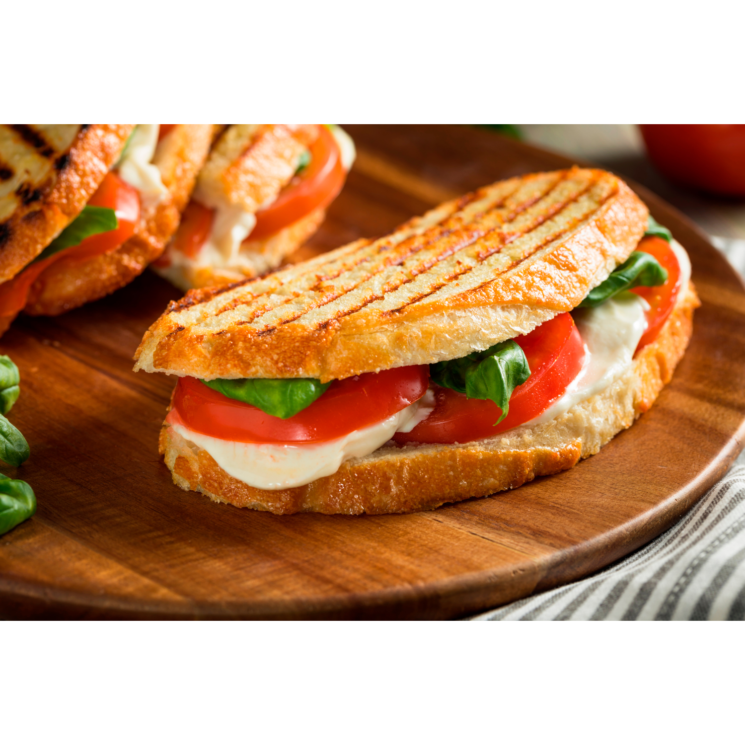 Grilled sandwich with tomato, mozzarella, and basil on a wooden board, close-up shot.