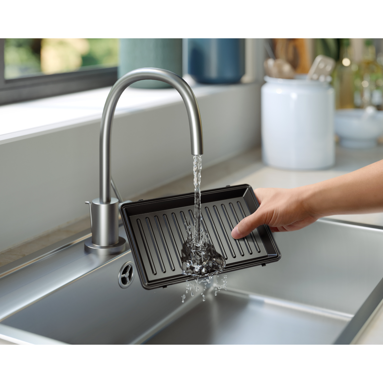 Water flows from a faucet into a black grill pan in a stainless steel sink.