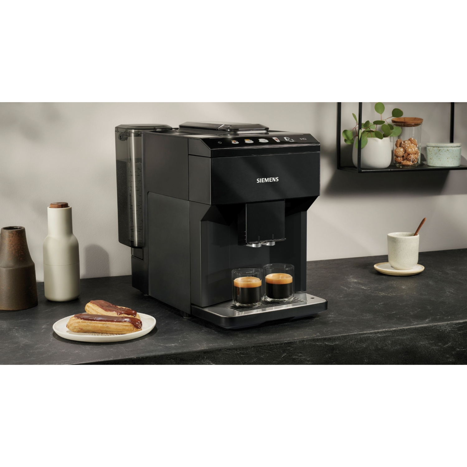 Black Siemens coffee machine with two espresso shots, pastries, and decor on a black counter.