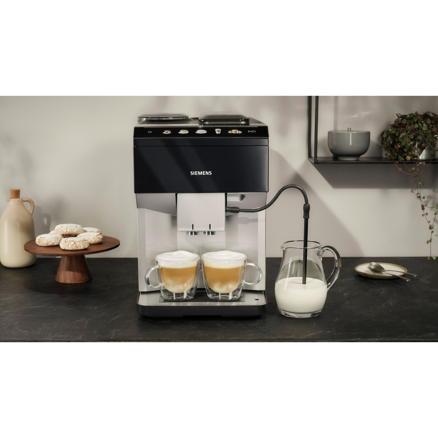Espressomachine met twee latte-kopjes en melkkan op een zwart oppervlak.