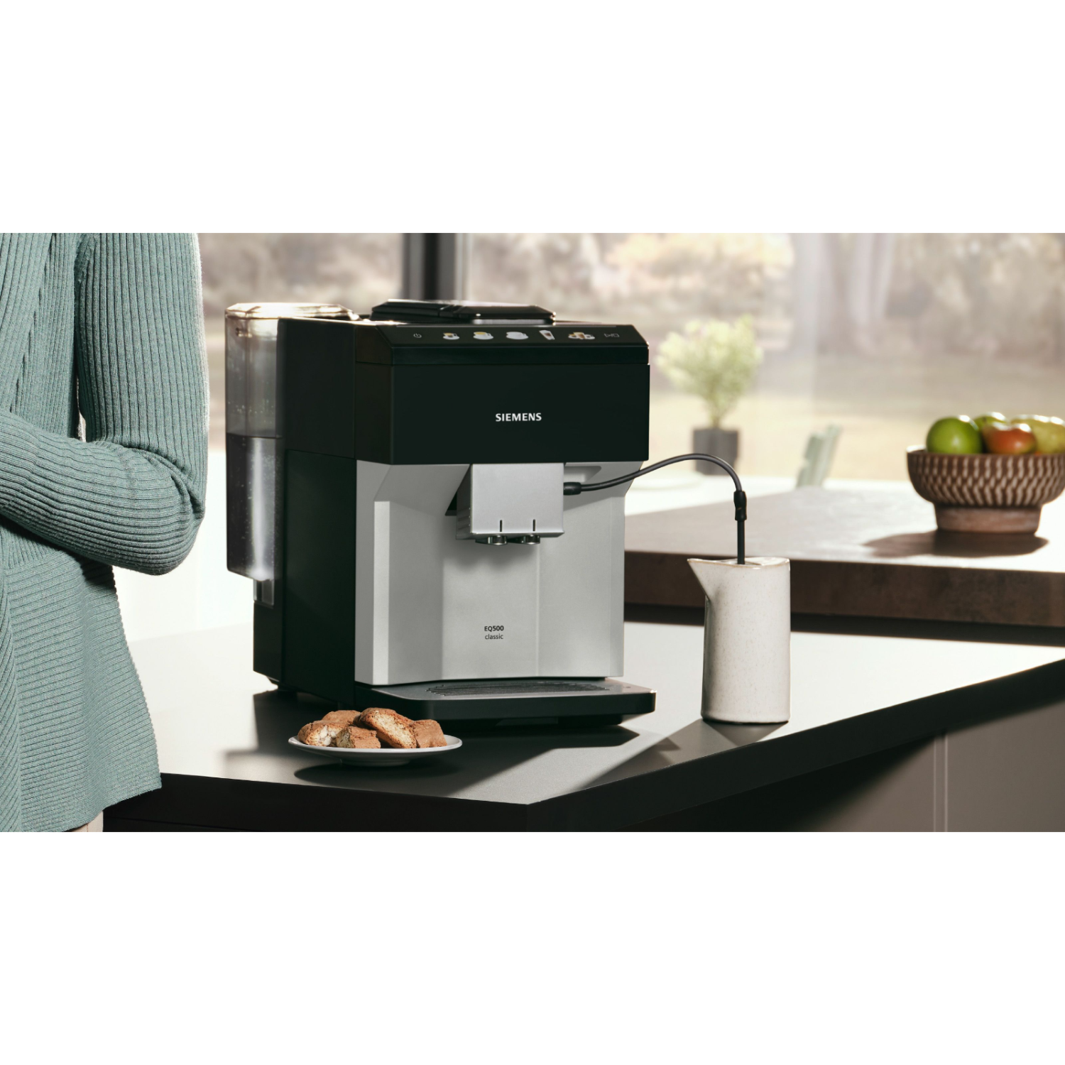 Een koffiemachine op een aanrecht naast een raam. Een persoon staat links.