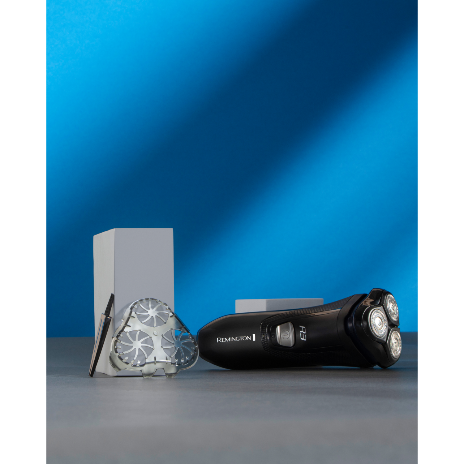 Black electric shaver with spare head, on a gray surface with blue and gray backdrop.