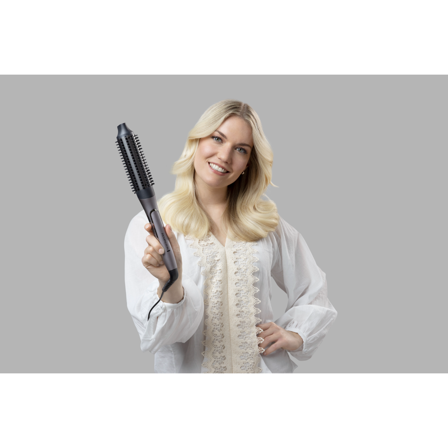 Een vrouw houdt een stylingborstel vast, lachend in de camera met blond haar.
