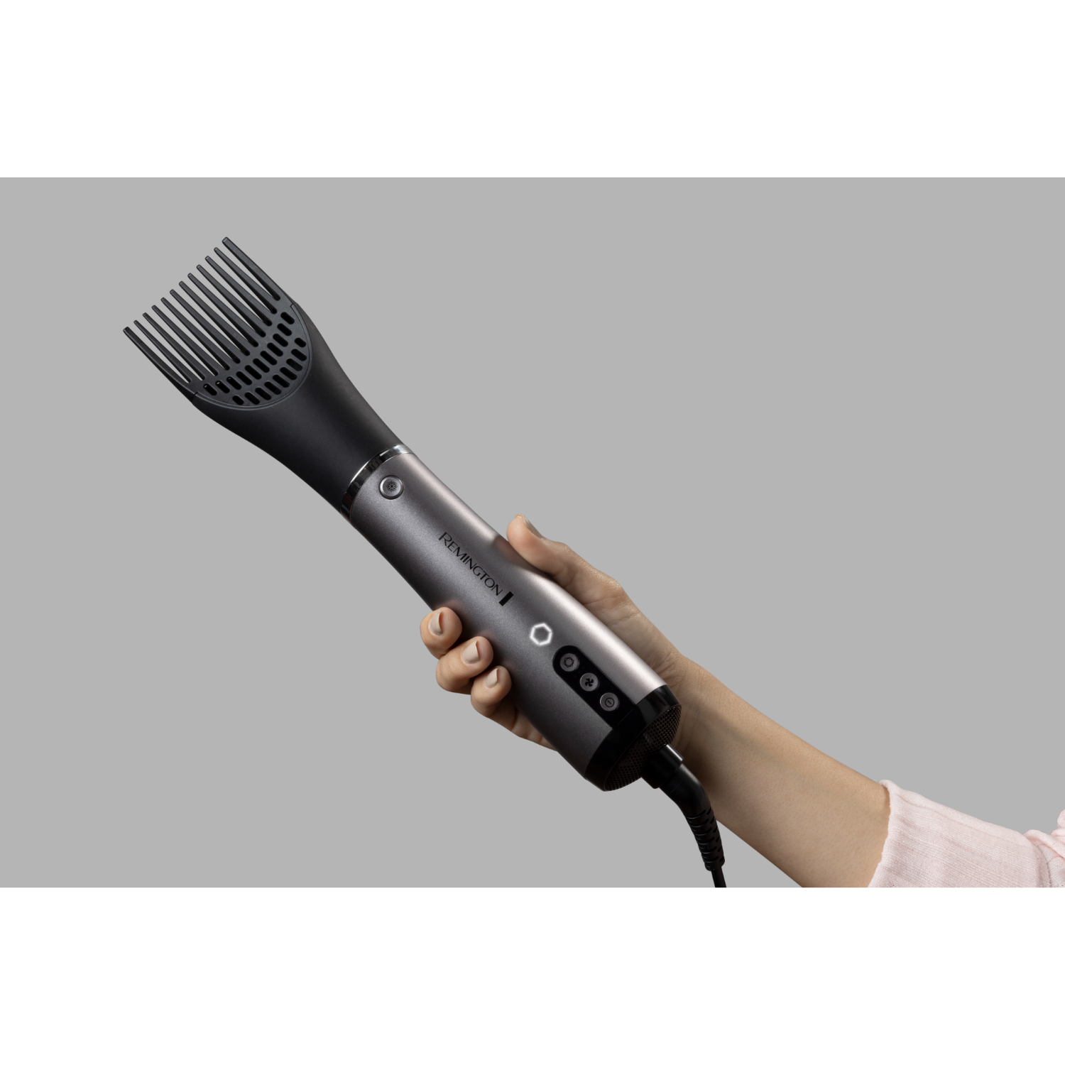 A black and gray hair dryer brush is held in a hand against a gray background.