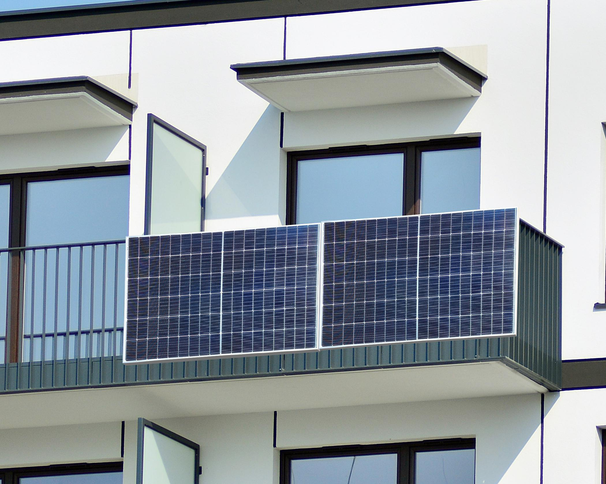 Ein modernes Gebäude mit Balkon mit Sonnenkollektoren. Fenster sind geöffnet, Paneele zeigen zum Himmel.