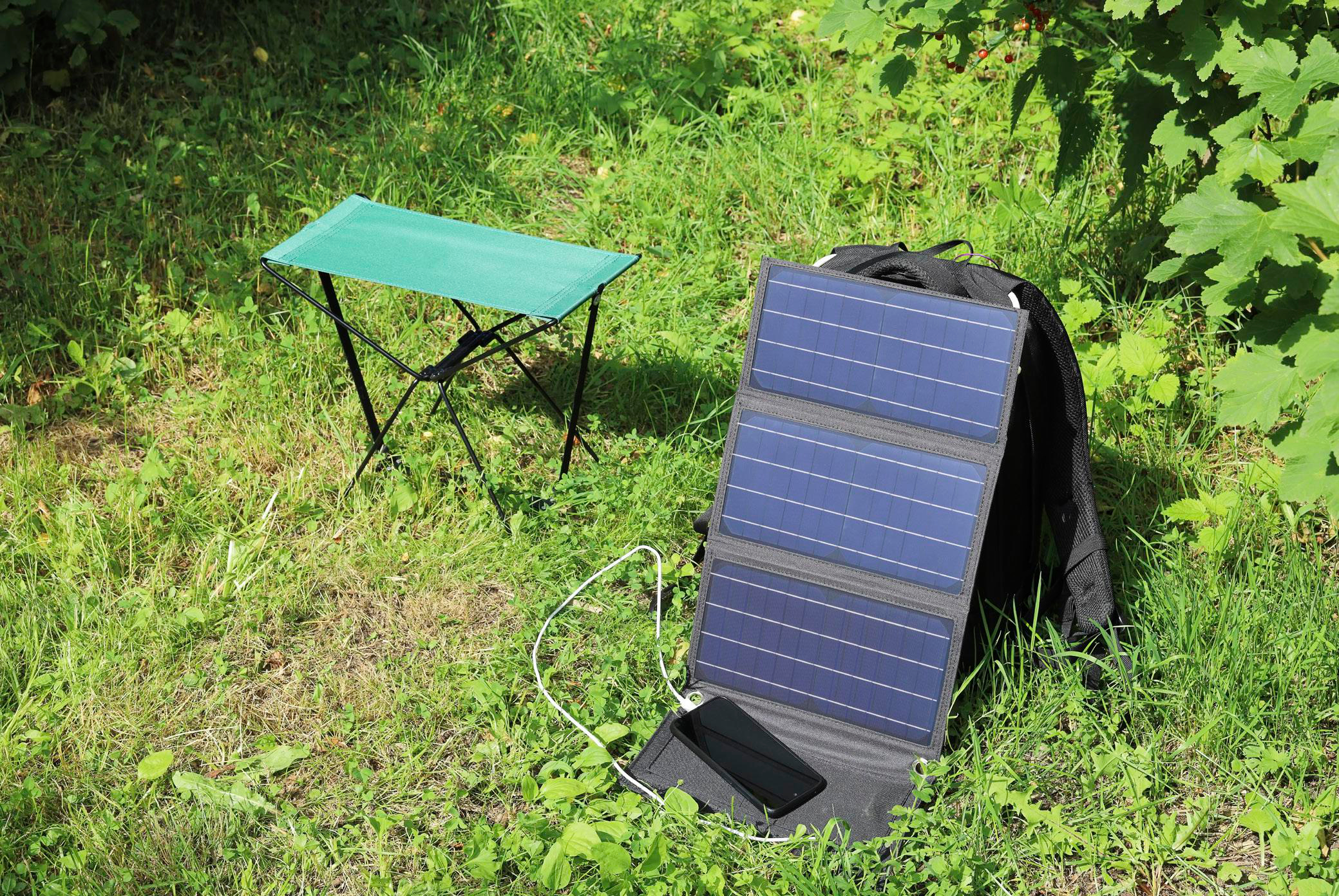 Ein Solarpanel mit schwarzem Rucksack, kleinem grünen Stuhl und Telefon.