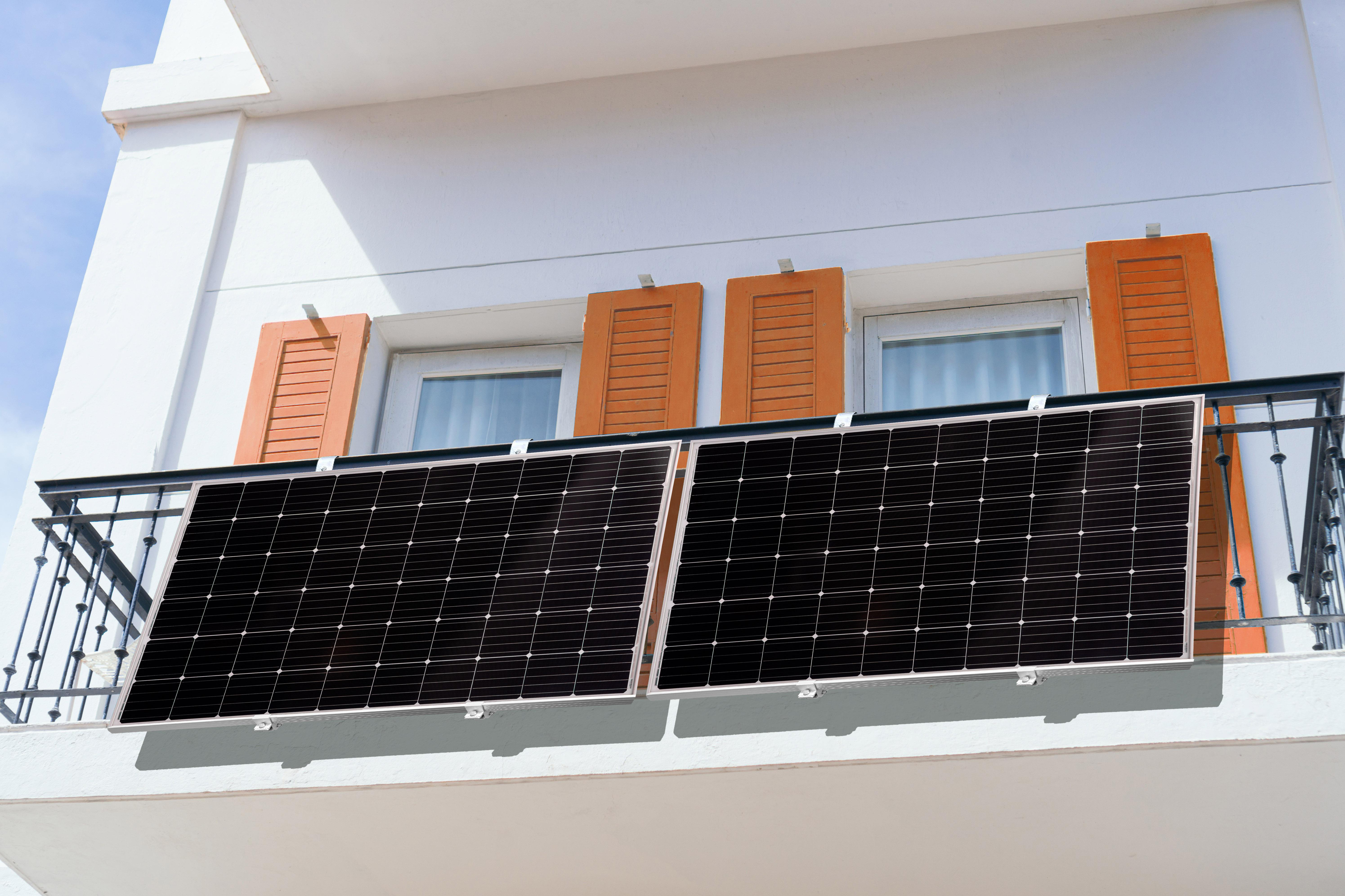 Zwei Sonnenkollektoren auf einem Balkon, weißes Gebäude mit orangen Fensterläden.