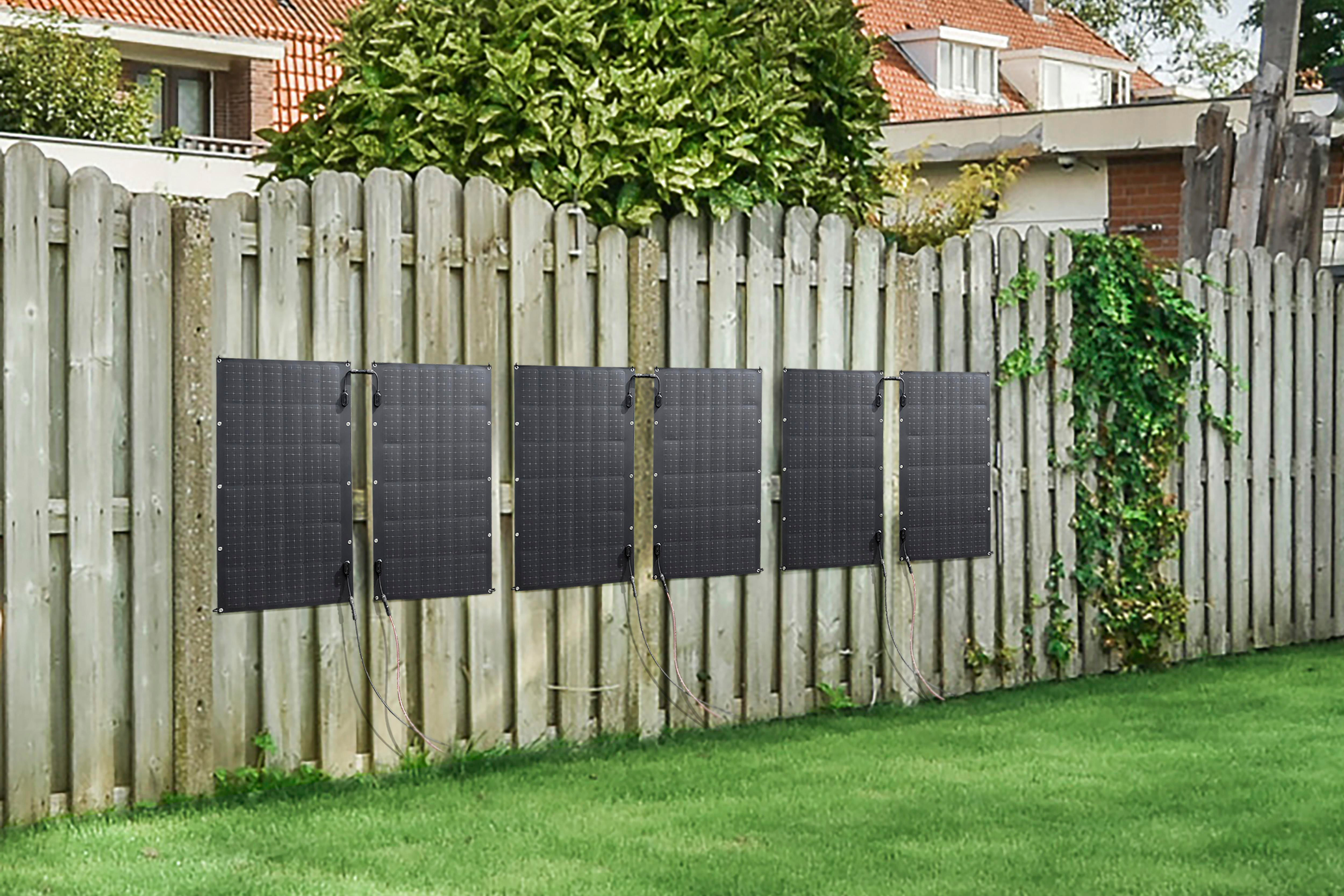 Solarpaneele auf einem Holzzaun, mit grünem Gras davor.