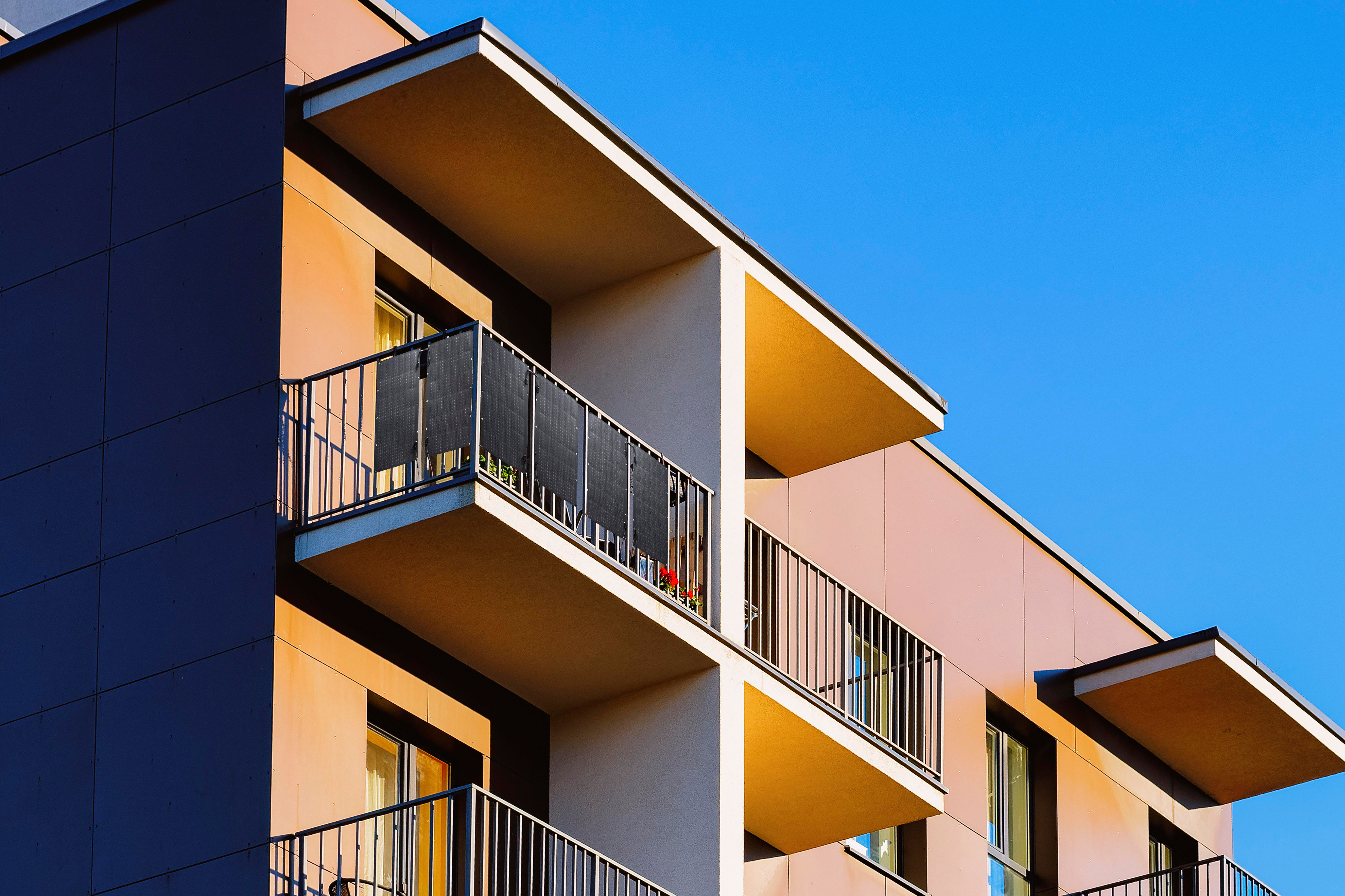 Wohnungsbalkone mit schwarzen Sichtschutzwänden und Metallgeländern. Blauer Himmel im Hintergrund.