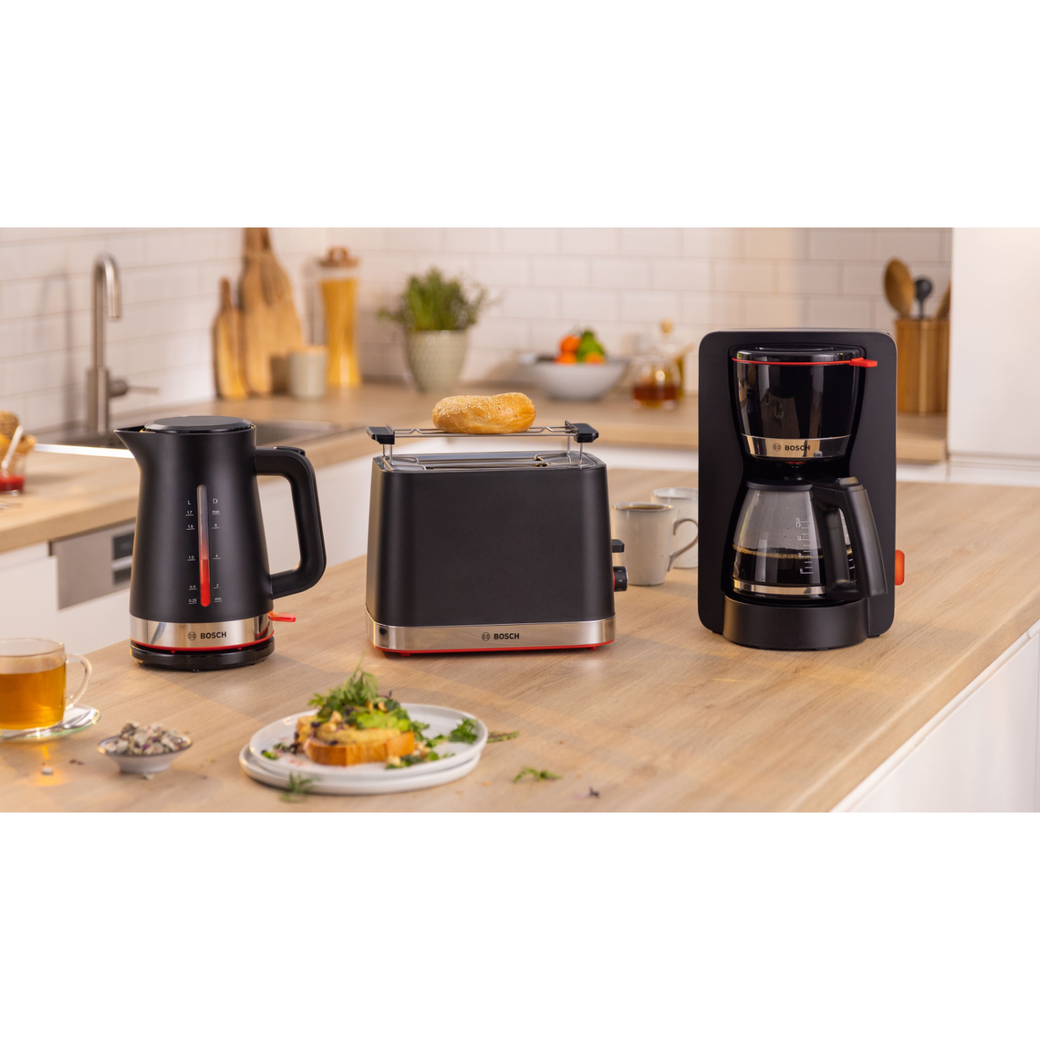 Zwarte en zilveren keukenapparatuurset: waterkoker, broodrooster en koffiezetapparaat op een houten aanrecht.