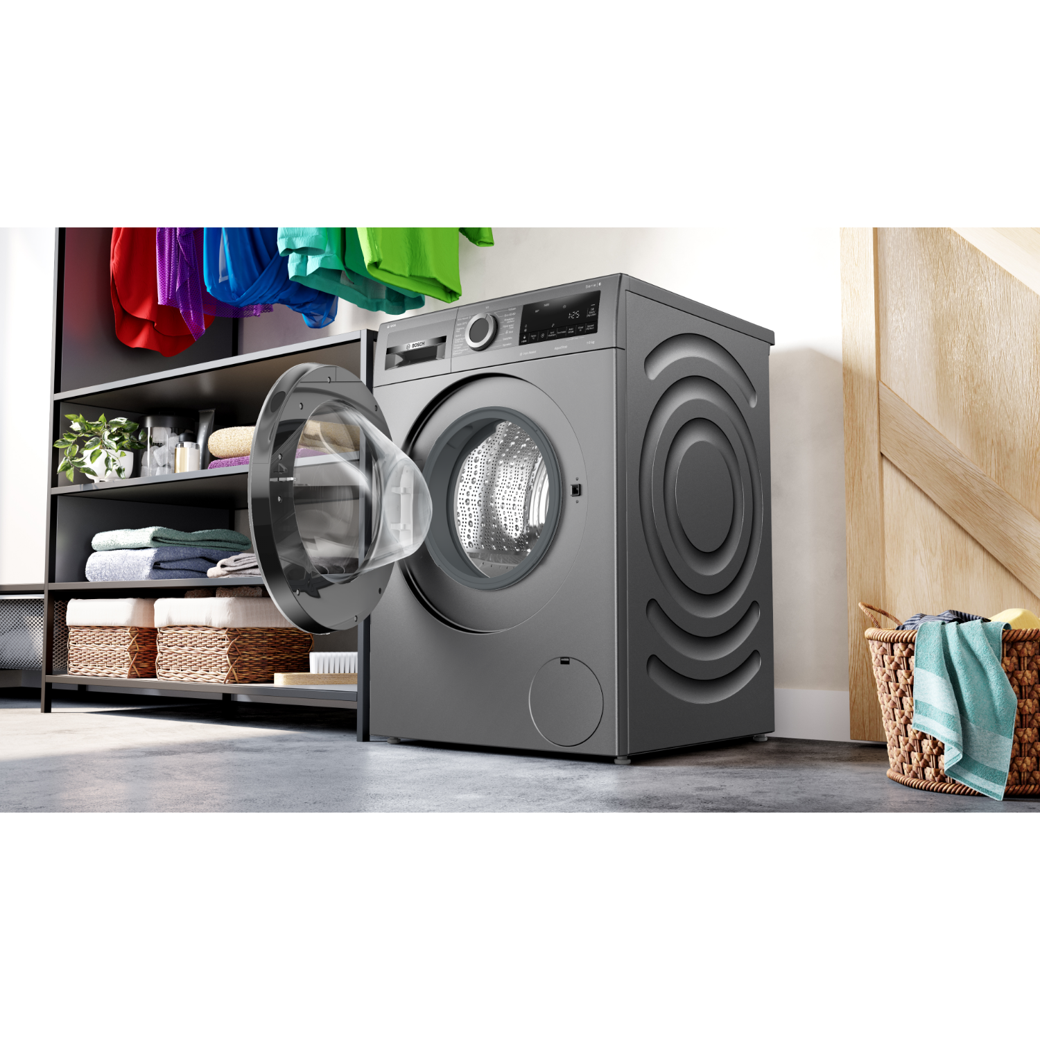 Een grijze wasmachine heeft de deur open. Wasgoed op rekken en een mand staan rechts.