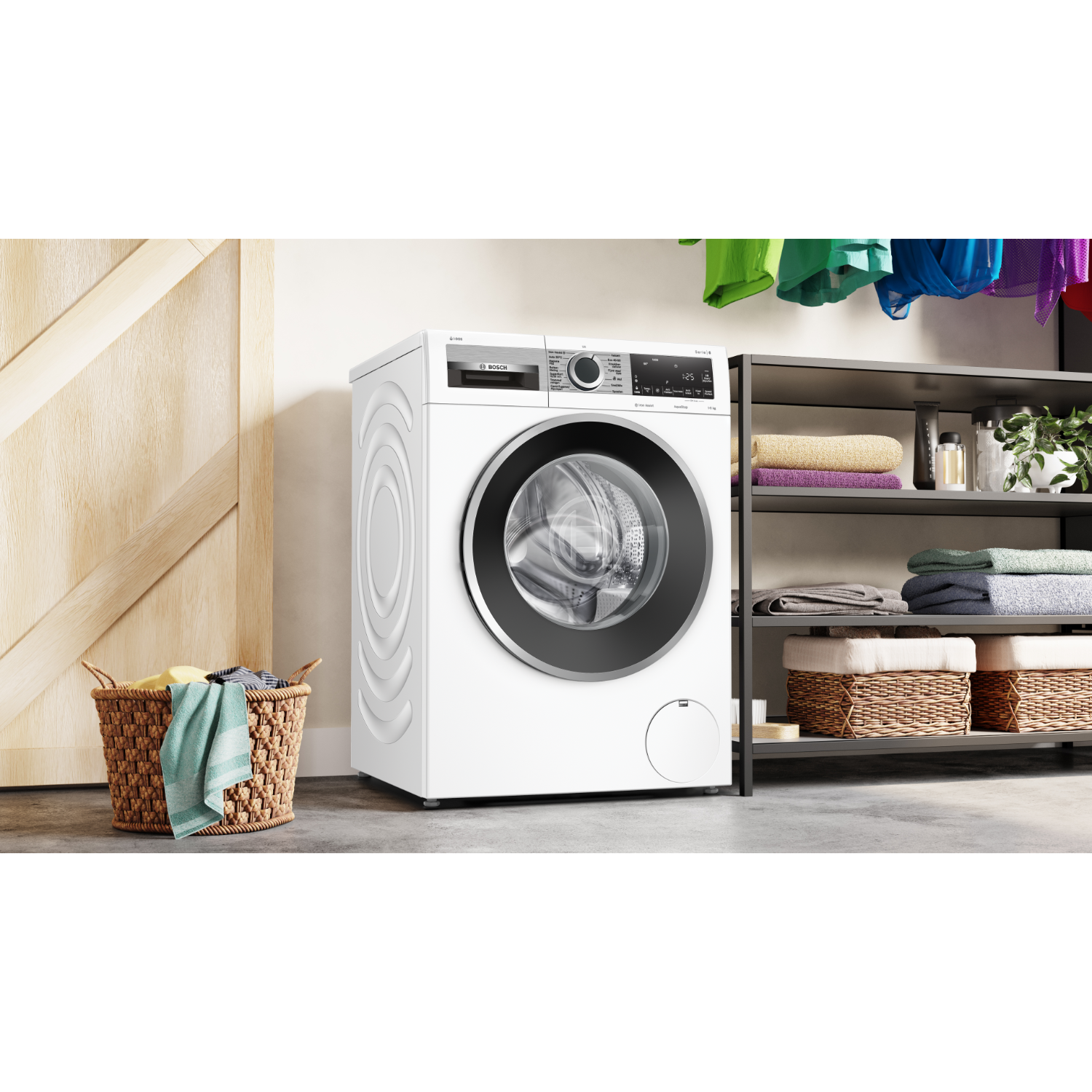 Een witte wasmachine naast een kast met kleding. Een mand met kleding op de voorgrond.