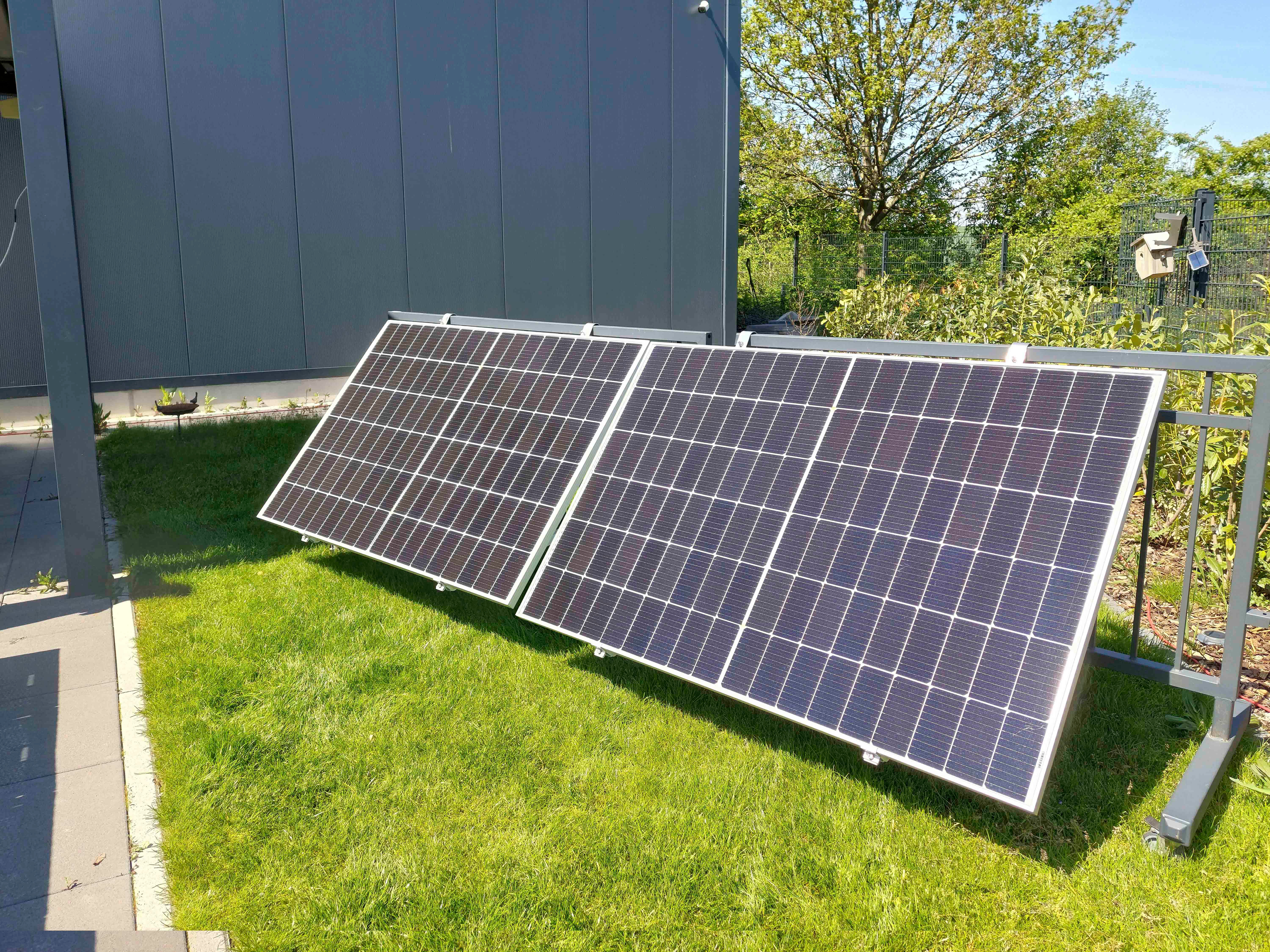 Zwei Solarmodule auf einem Metallrahmen, platziert auf grünem Gras vor einem grauen Gebäude.