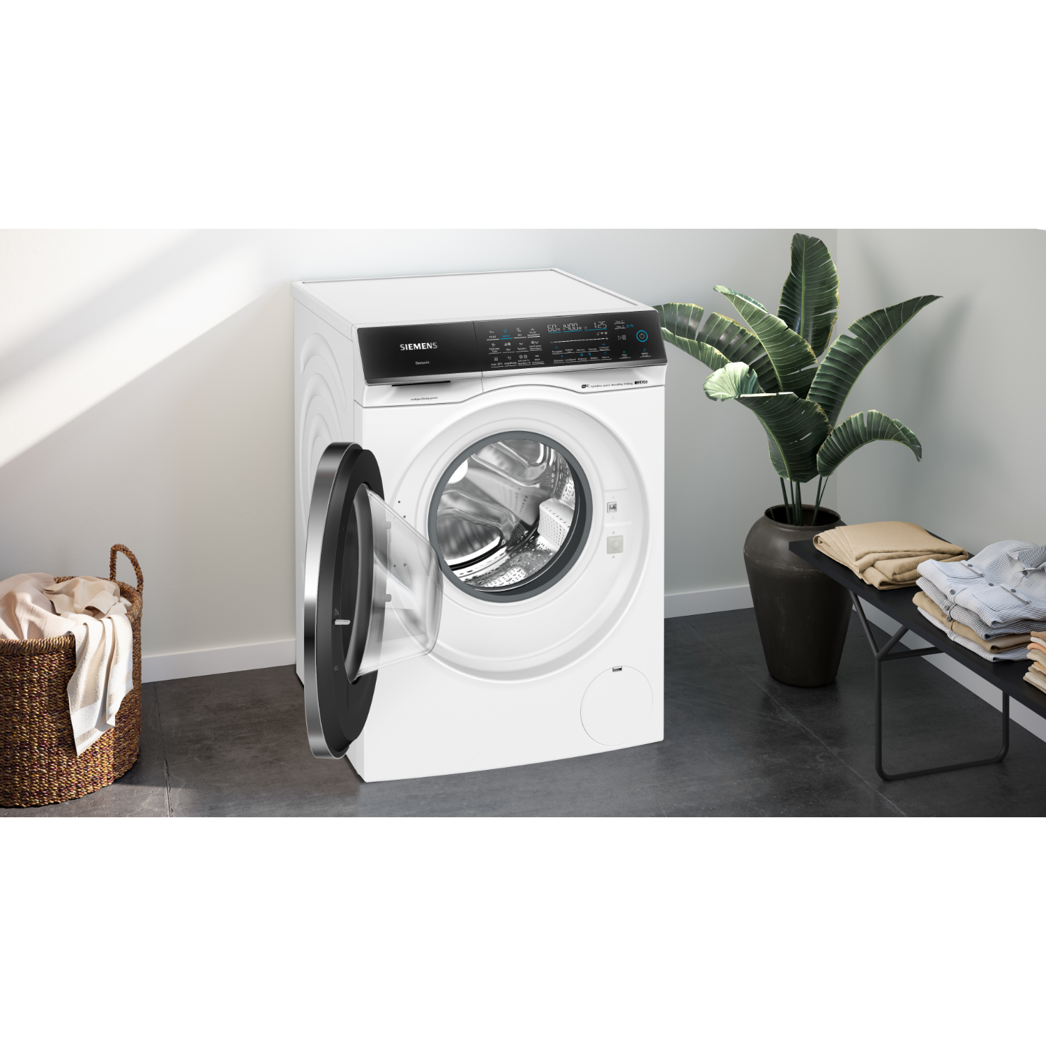 A white washing machine with the door open. Beside it is a basket of clothes and a plant.
