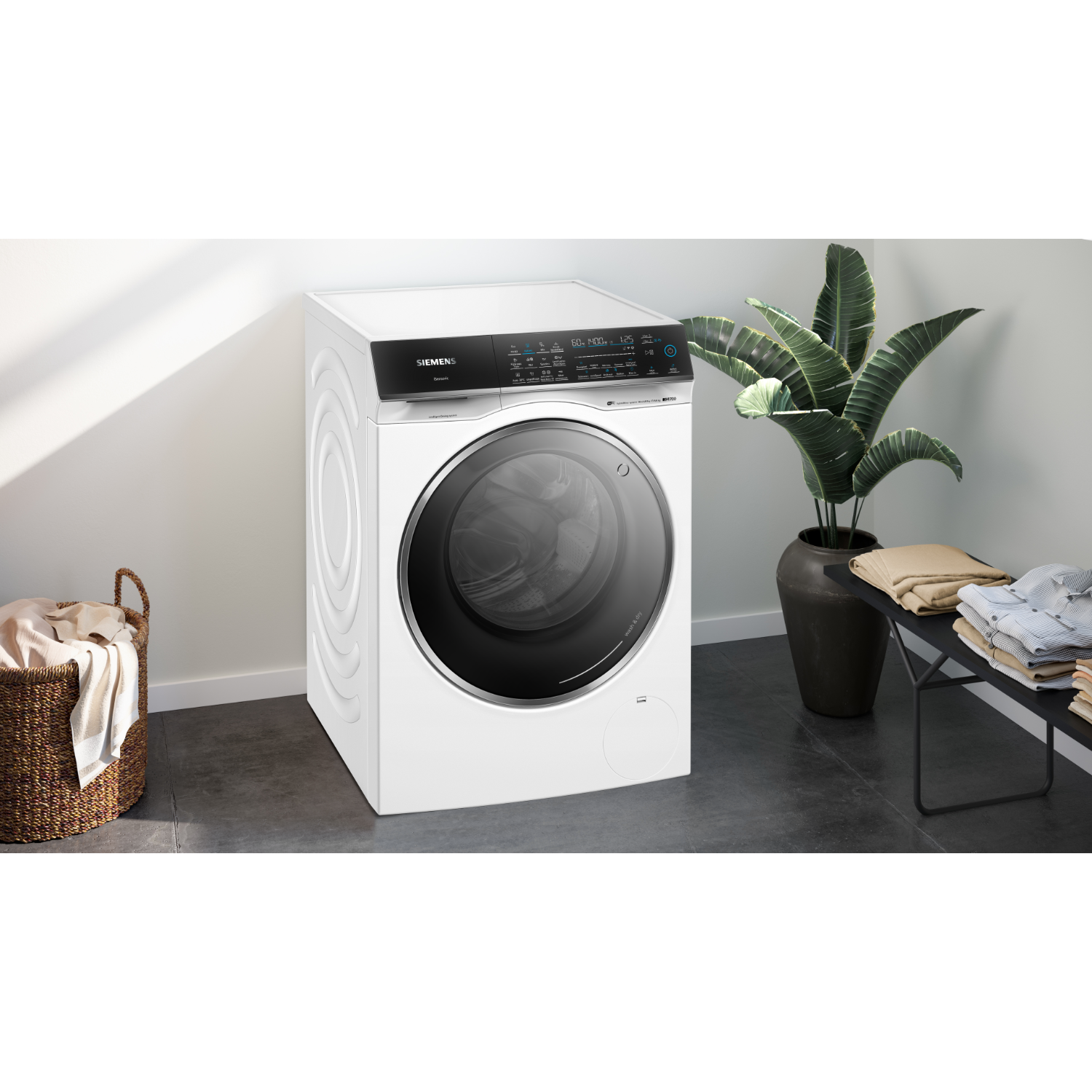 White washing machine in a laundry room. A clothes basket and plant are to the left and right.