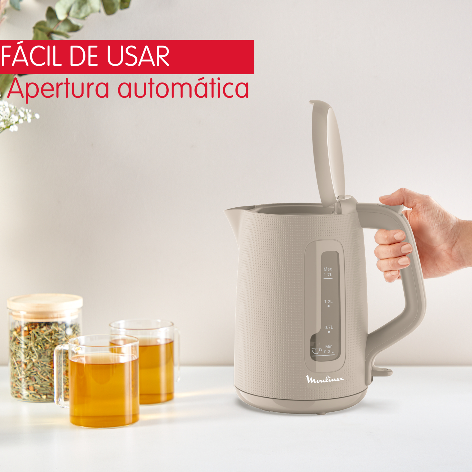 Una tetera eléctrica beige con la tapa abierta. Una mano sostiene el asa.
