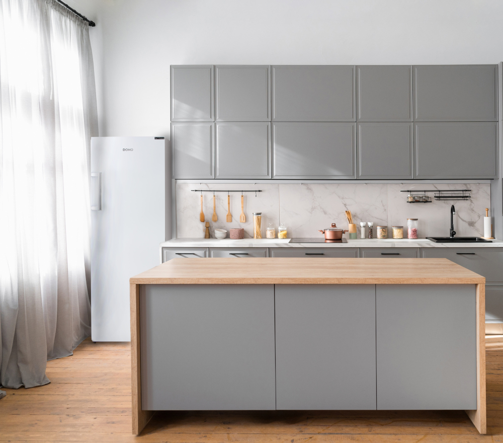 Modern kitchen interior with a gray island, cabinets, and white fridge on the left.