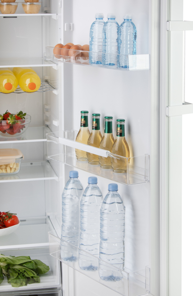 The inside of a refrigerator with food items, including bottles, eggs, and tomatoes.